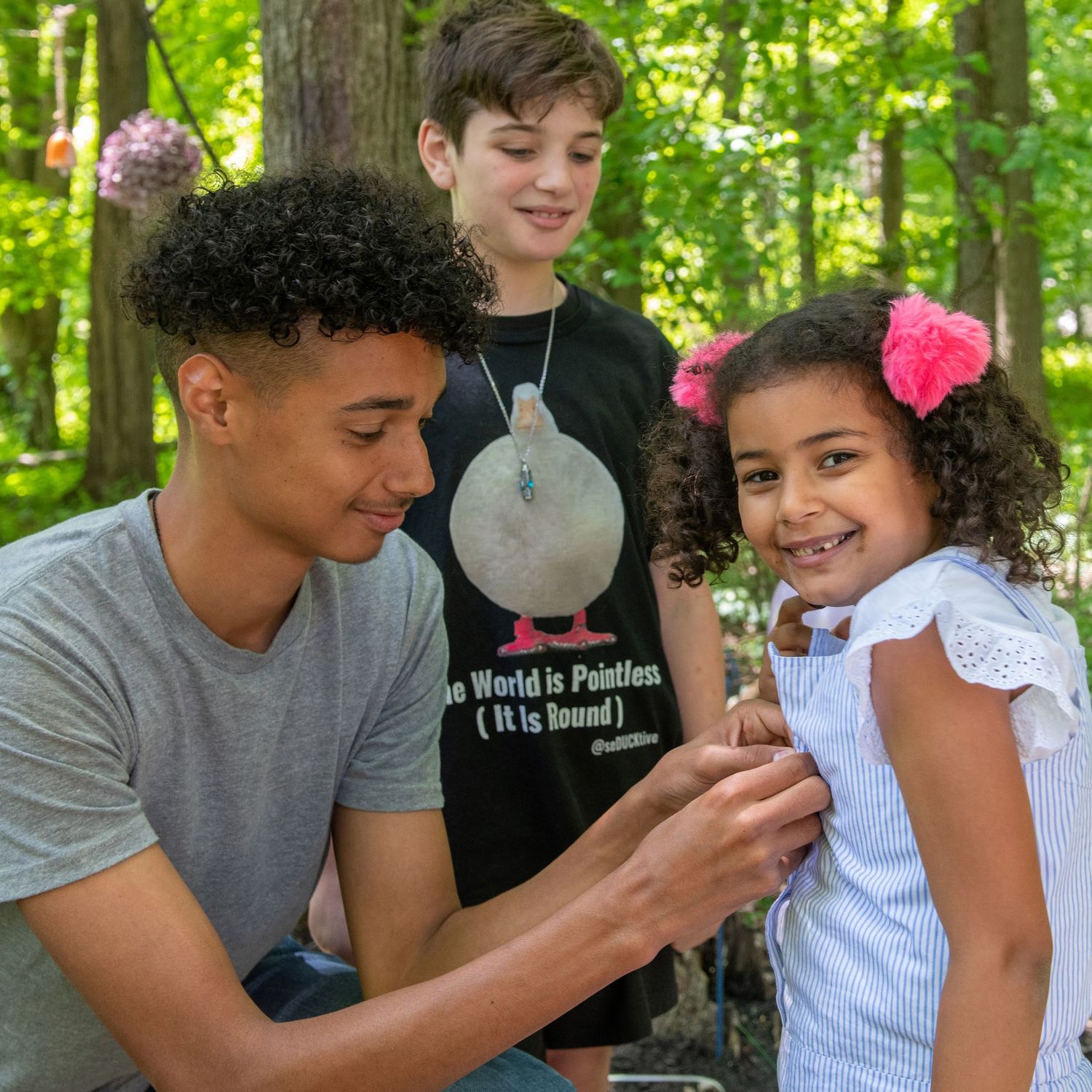 People interacting together outdoors in a wooded setting with sunlight filtering through trees.