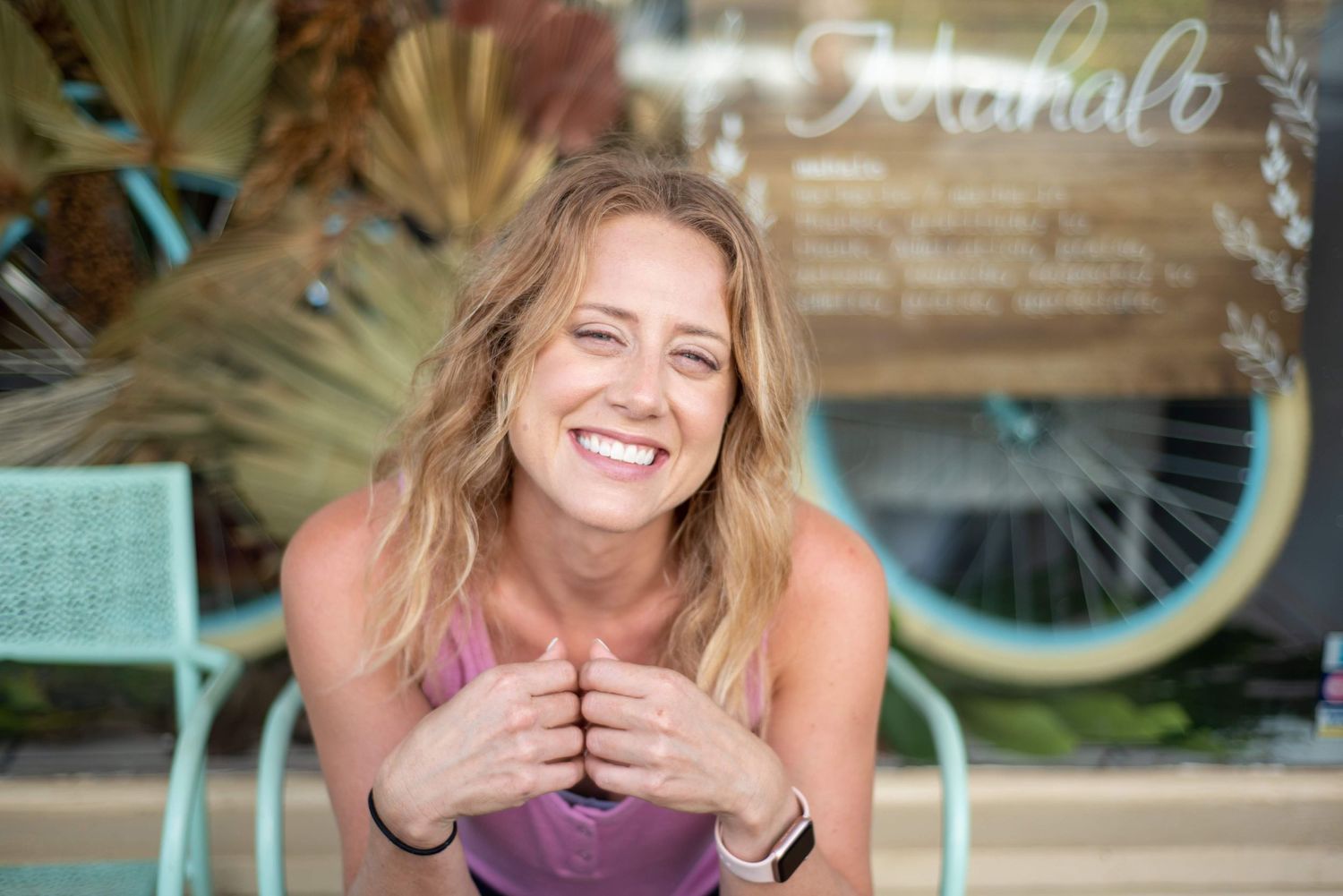 Person laughs joyfully while sitting at outdoor cafe with mint green chairs and vintage bicycle in background.