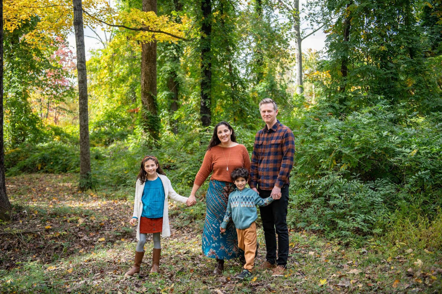 Family of four poses together in autumn forest setting with golden foliage.