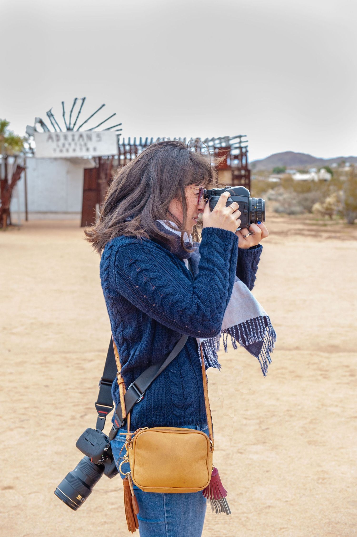 Photographer in blue sweater takes photos in desert landscape with vintage signage.