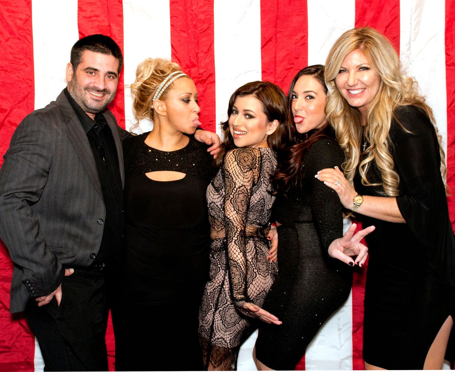 Group photo against red and white striped backdrop with people in formal black attire.