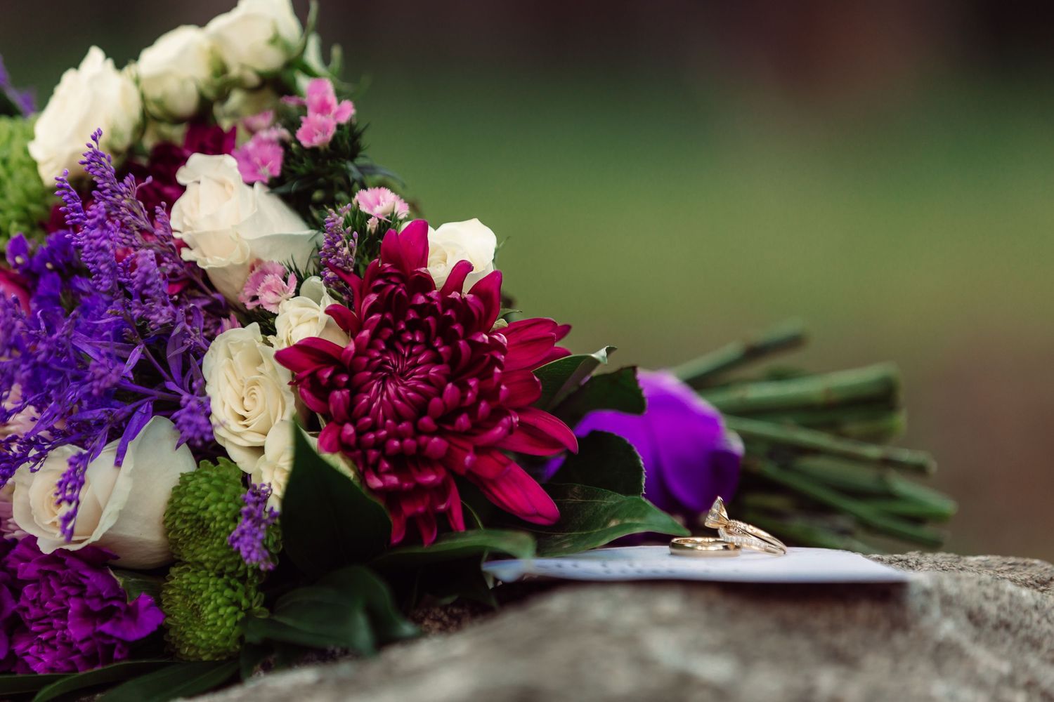 A vibrant wedding bouquet featuring purple, burgundy and white flowers on stone.