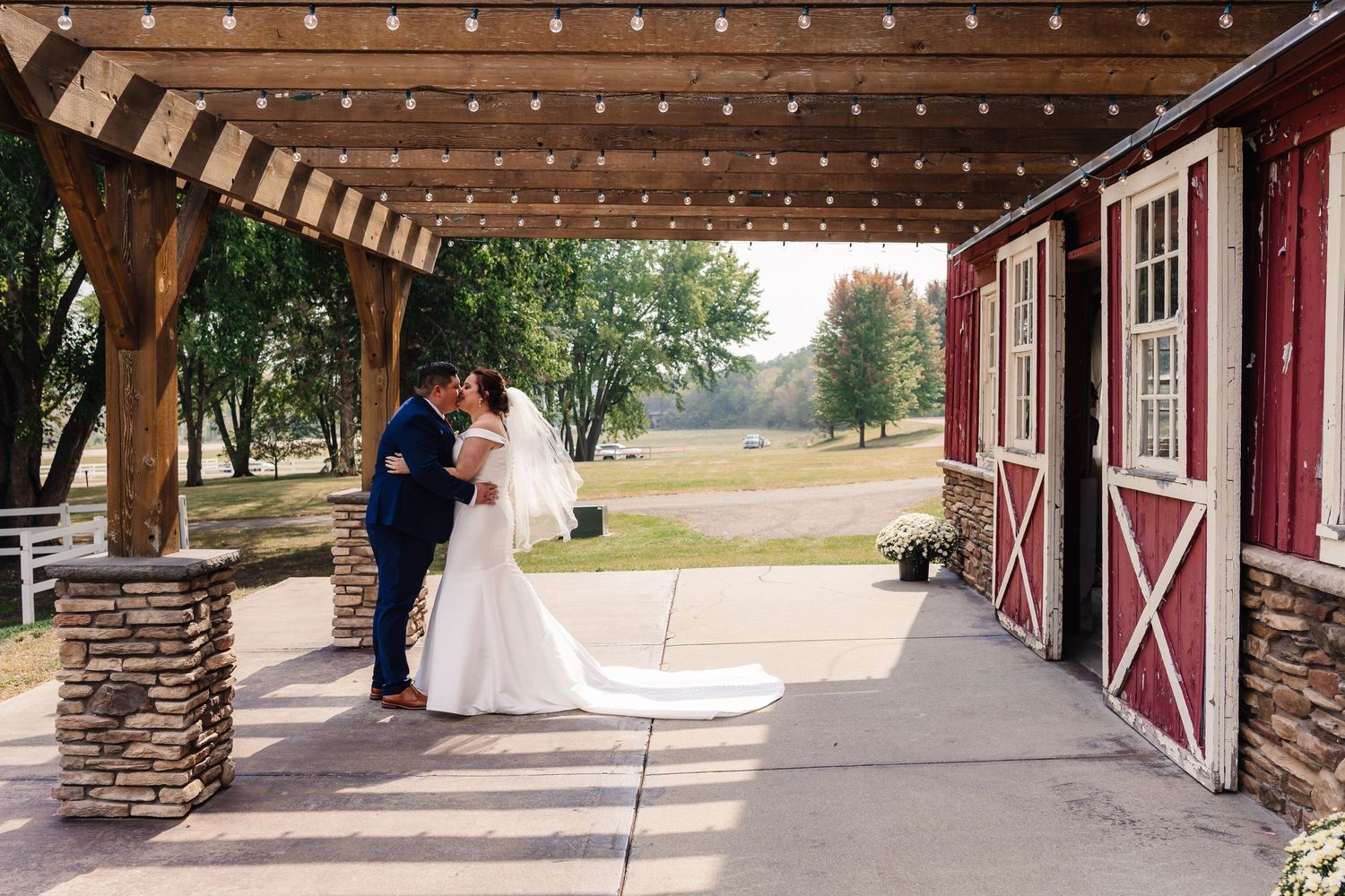Bride and groom sharing an intimate moment outside a red barn with string lights.