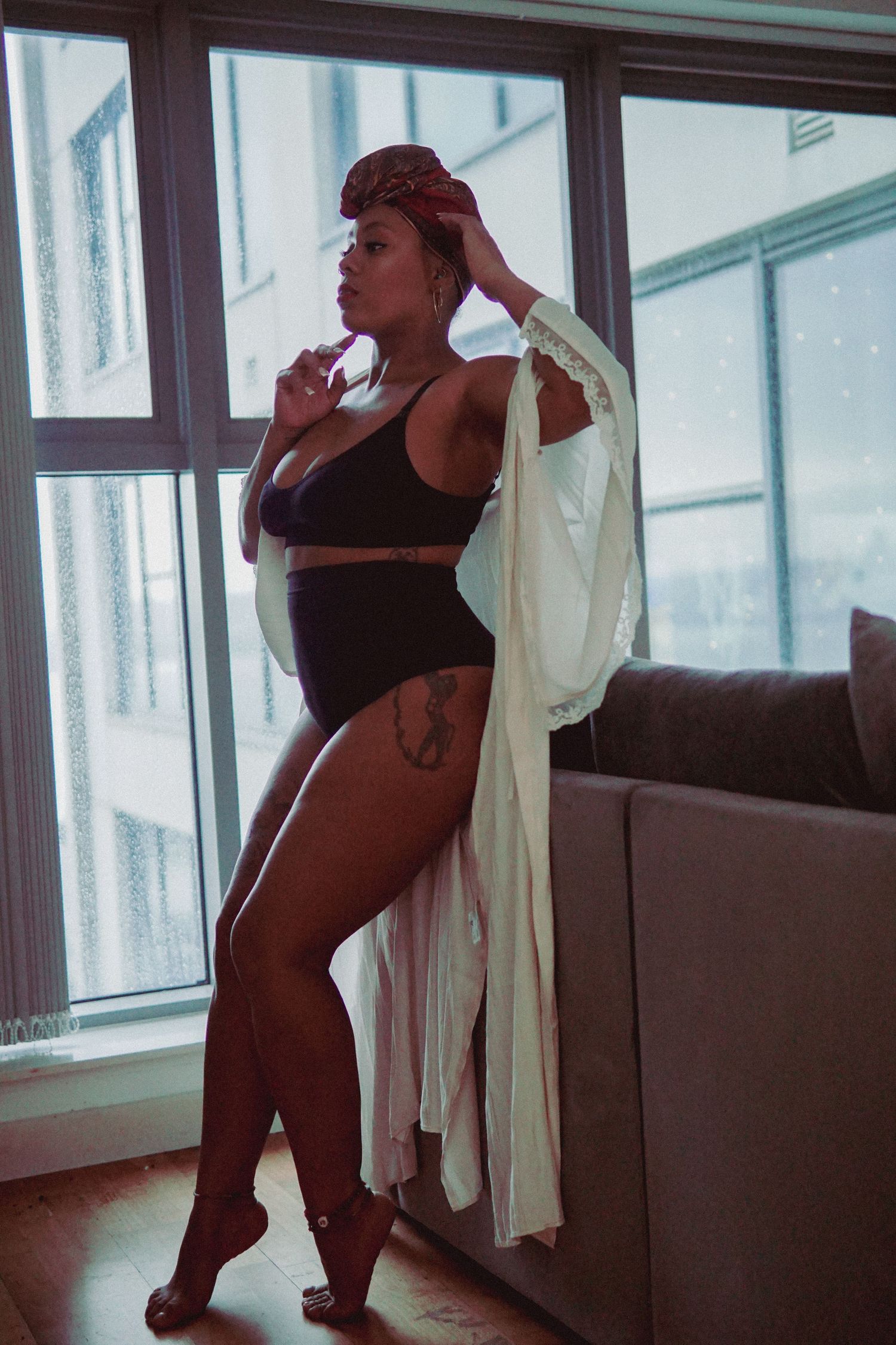 Woman with red headscarf, black matching underwear set and white silky robe posing on a edge of sofa Boudoir photography UK Liverpool