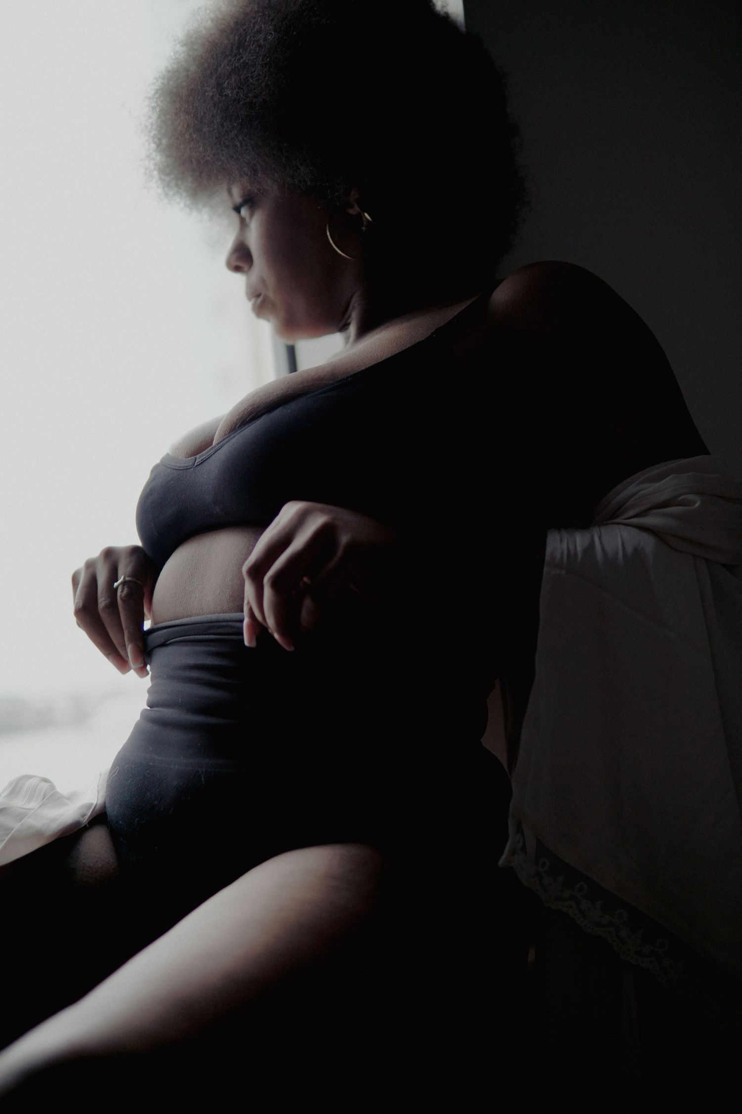 Woman with afro and black matching lingerie sitting on window and looking out of window Boudoir photography UK Liverpool