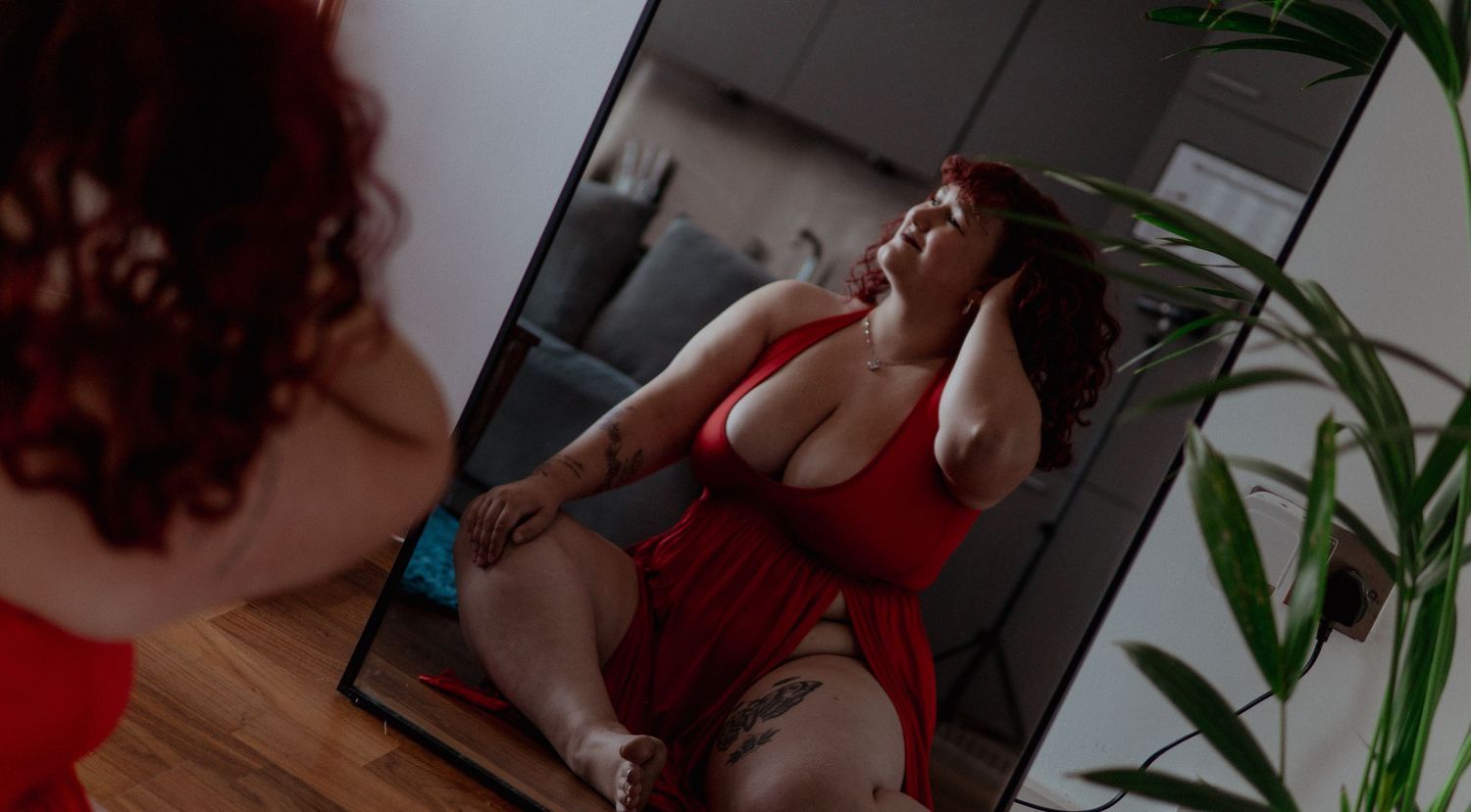 Mirror reflection of a woman in red dress sitting on a floor. Boudoir photography UK Liverpool