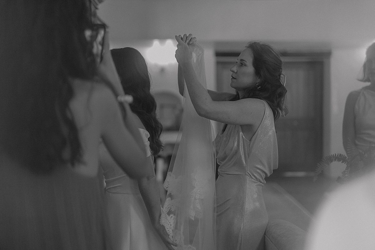 Candid moment of bride and bridesmaids helping with dress and veil