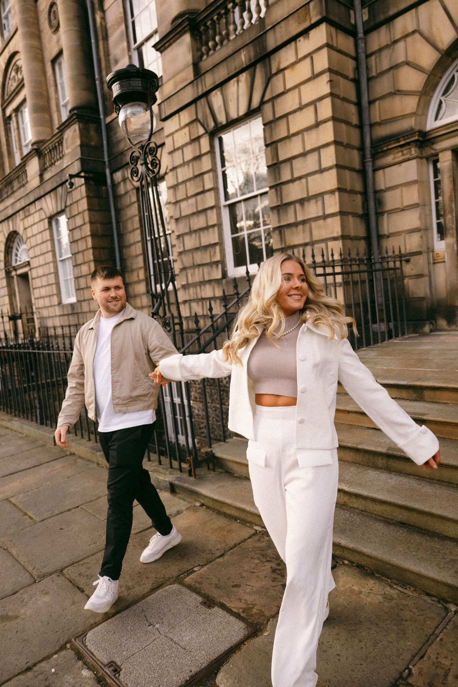 A stylish couple in coordinated outfits walking along historic city streets.