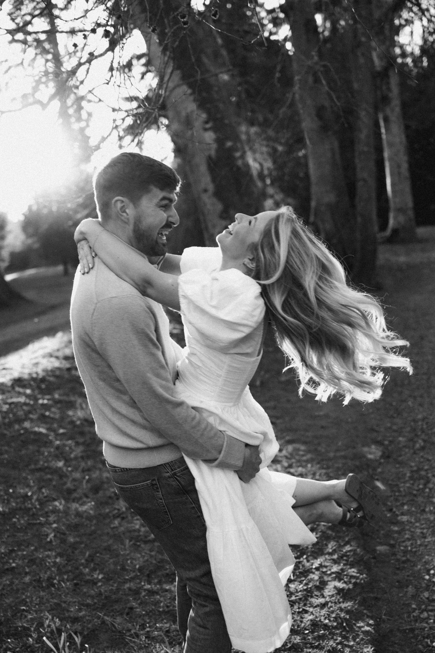 A romantic black and white photo of a couple embracing in a wooded setting.