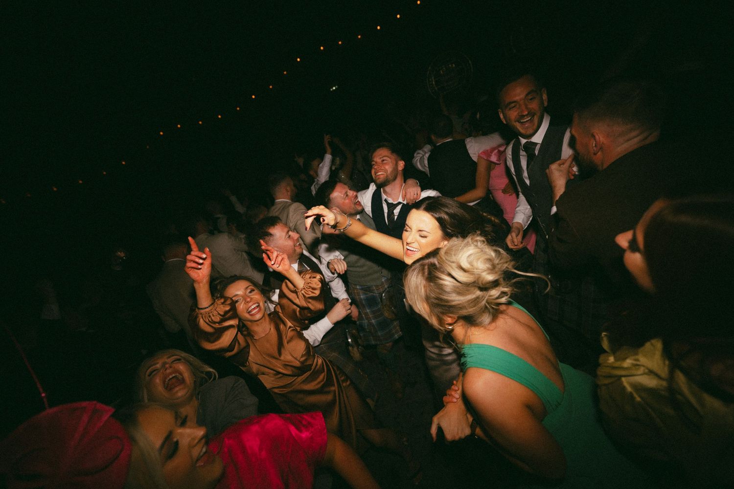 A crowded group of partygoers dancing enthusiastically in a dark nightclub with dramatic lighting.