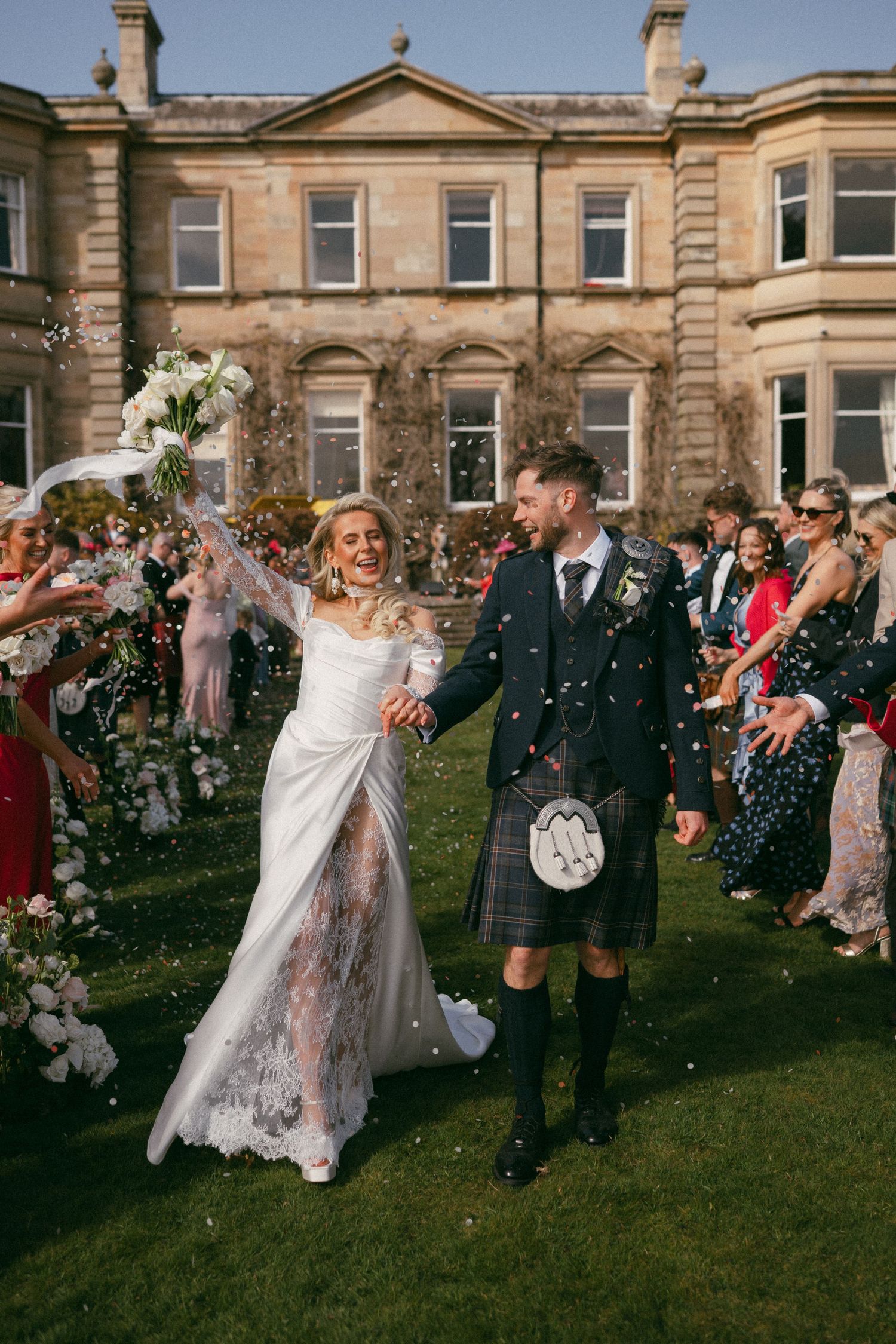 Newlyweds celebrate with guests throwing confetti outside a grand Scottish manor house during their traditional wedding ceremony.