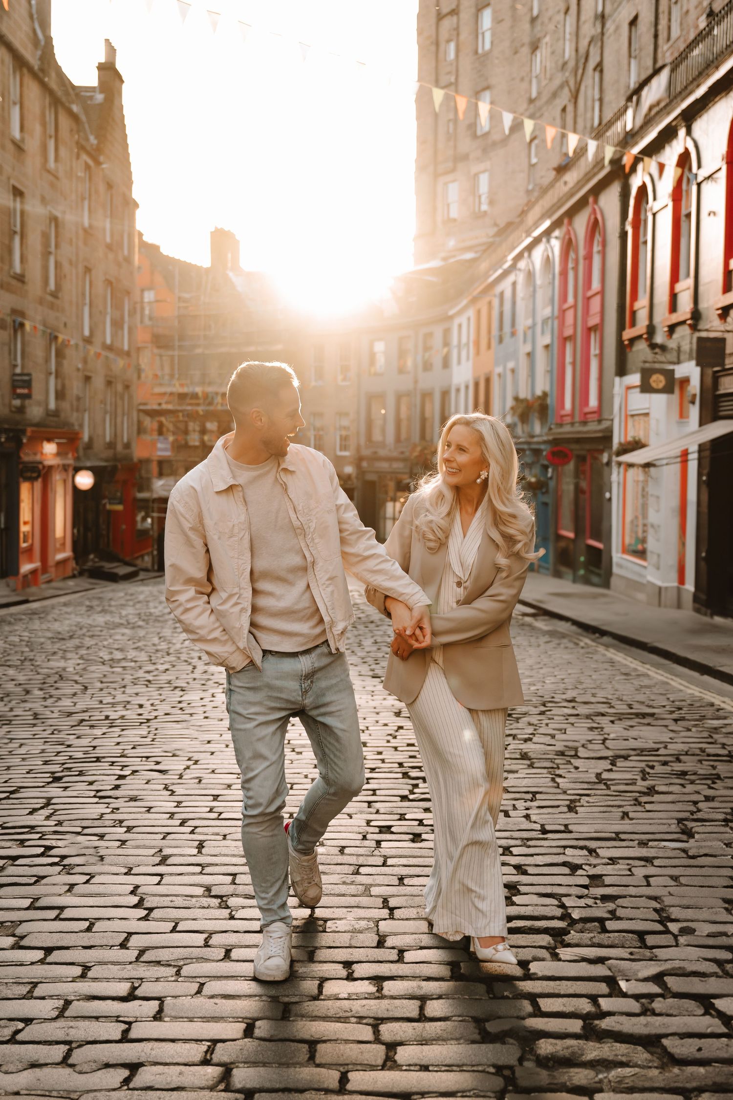 A couple walking hand in hand on cobblestone streets during golden hour.