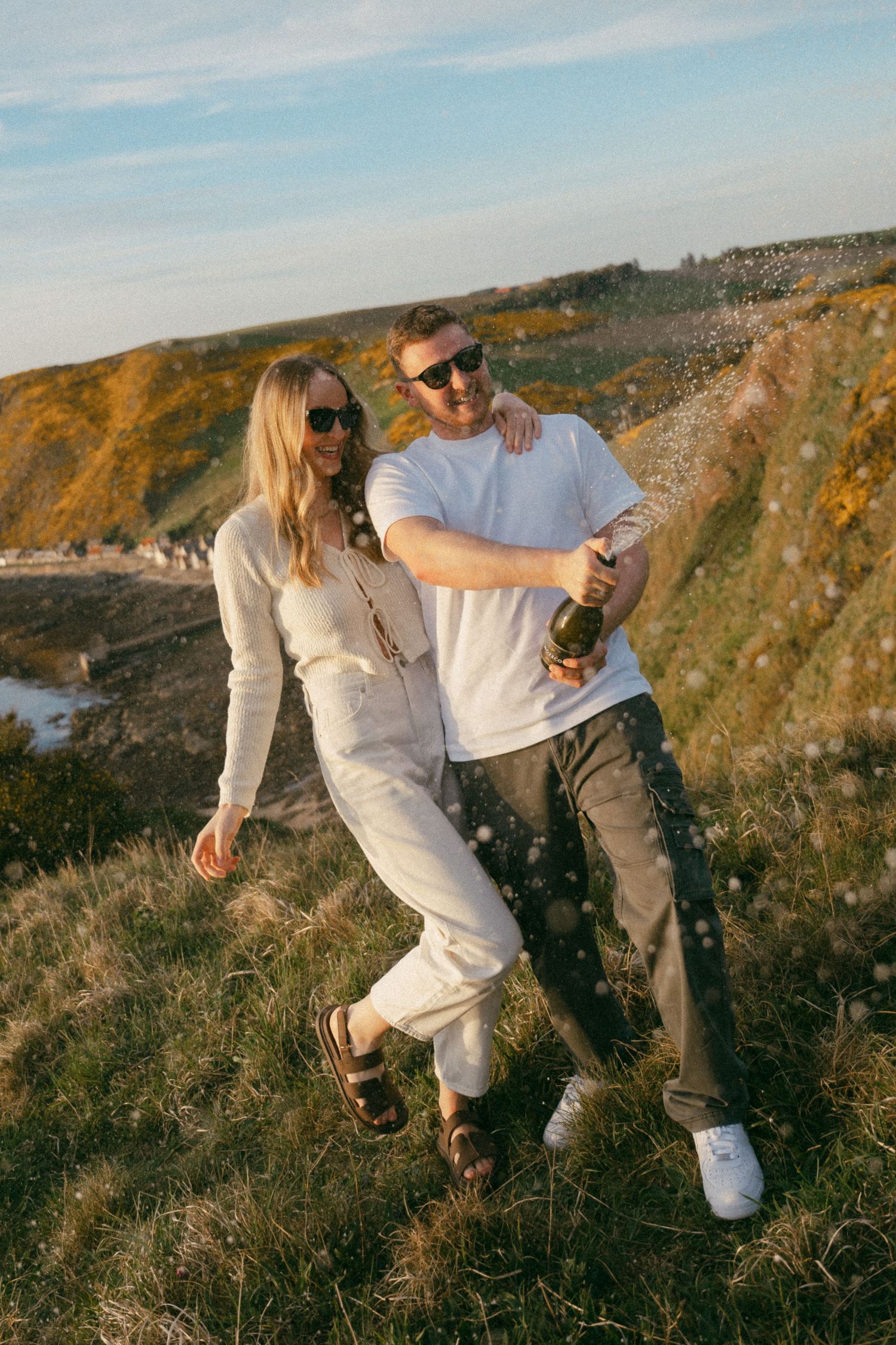 A casual couple in white outfits enjoying a sunny day on coastal cliffs.