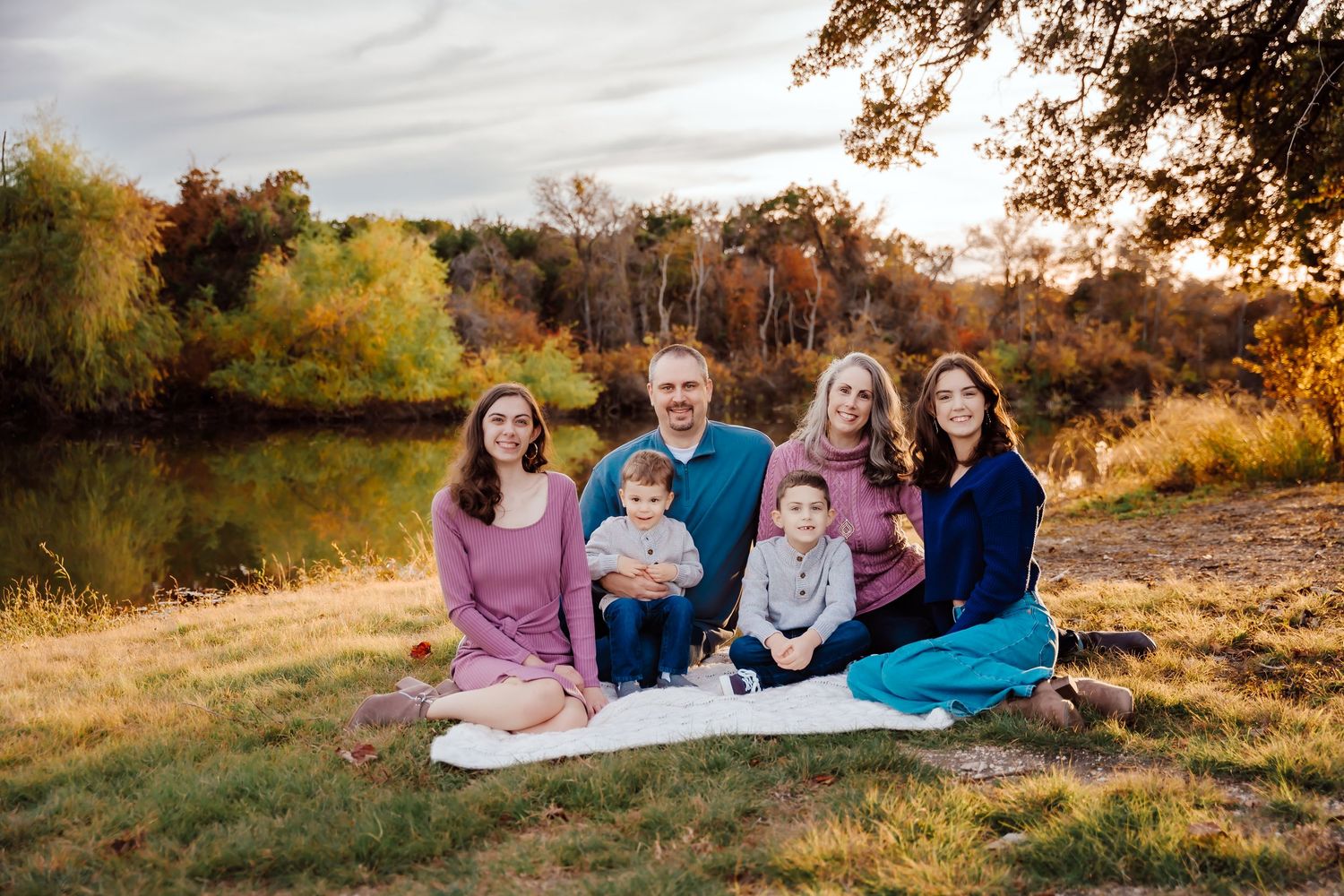 Beautiful family photo session in a golden autumn field at sunset with warm natural lighting and fall foliage.