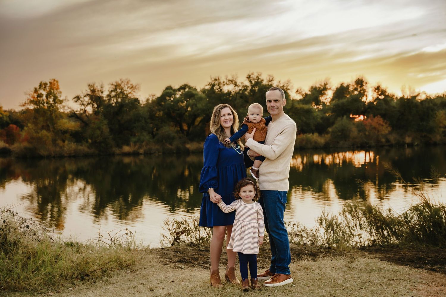 Couple sharing tender moments by a serene lake at sunset with golden light reflecting on calm waters.