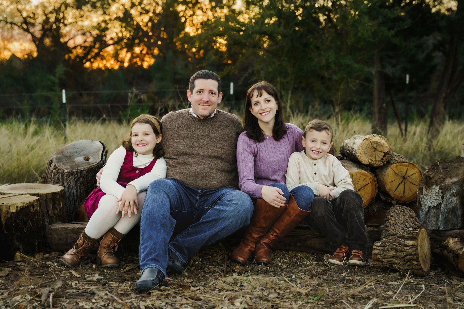 People sitting outdoors at sunset in a cozy group amidst golden fall foliage and wooden logs.