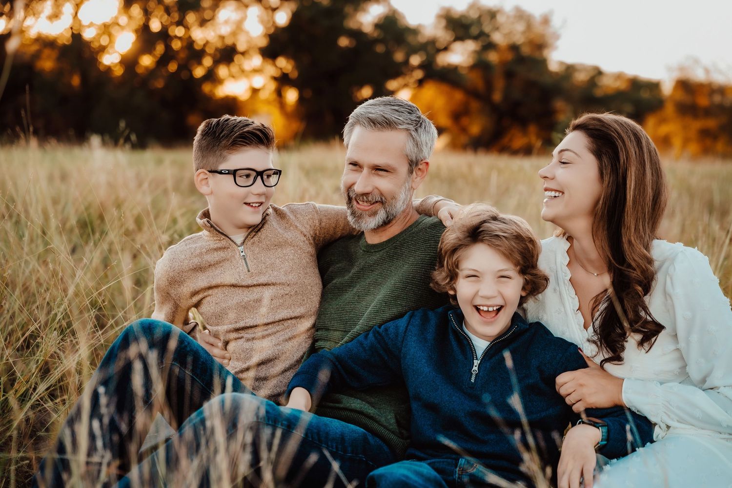 A family sitting together in a golden field during sunset, sharing joyful laughter as they embrace.