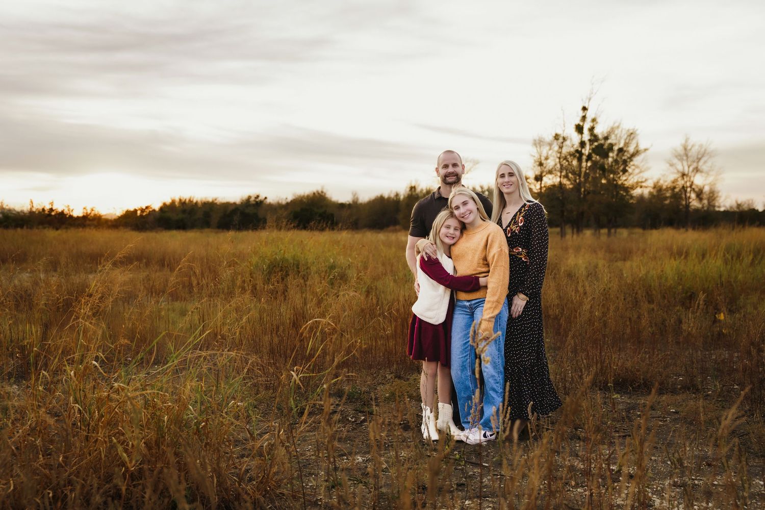A group of people pose together in a golden autumn field during sunset with trees in the background.