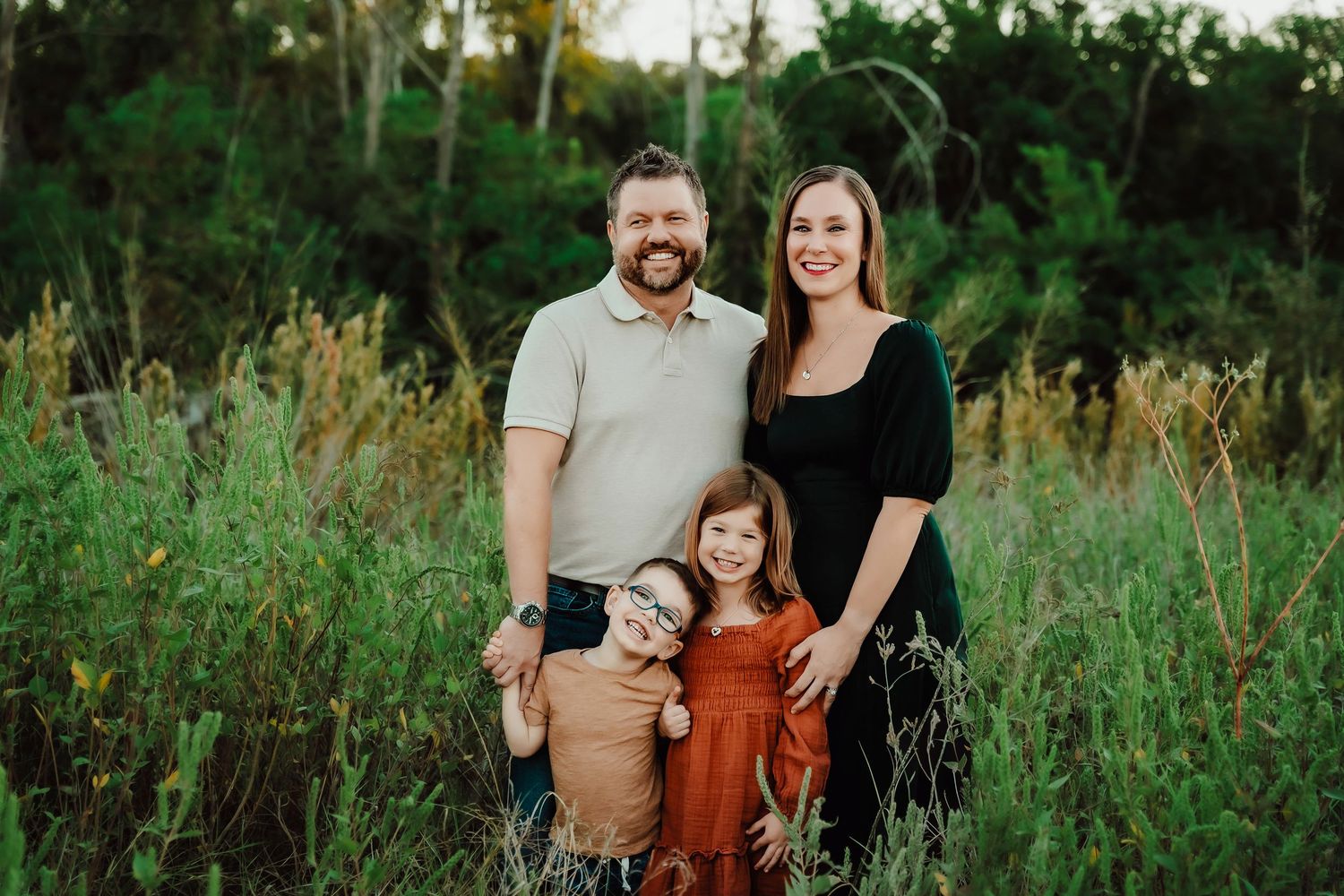A group poses together in a nature setting with tall grass and trees at sunset.