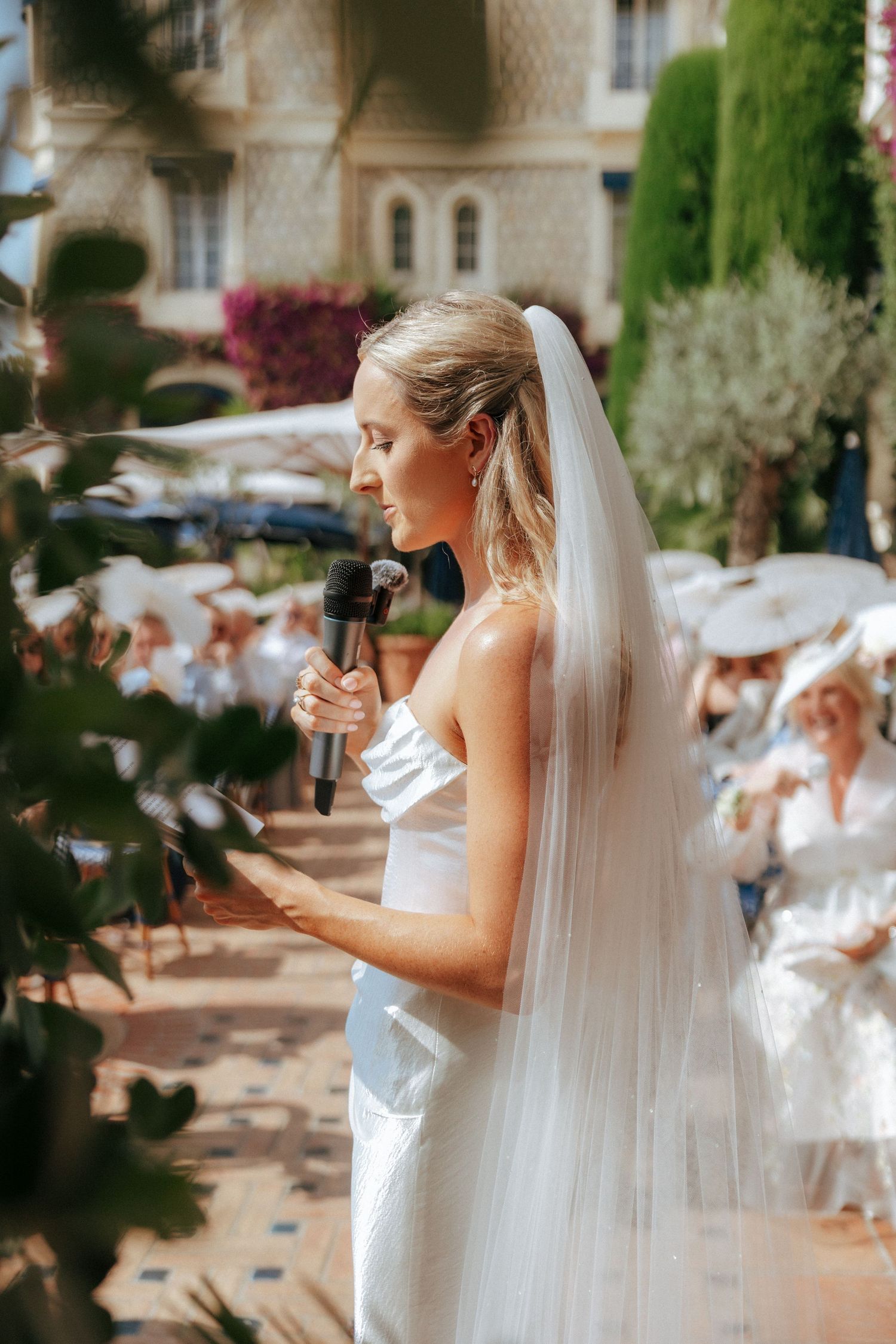 Sun-drenched outdoor wedding ceremony with white-dressed attendees and vibrant bougainvillea.