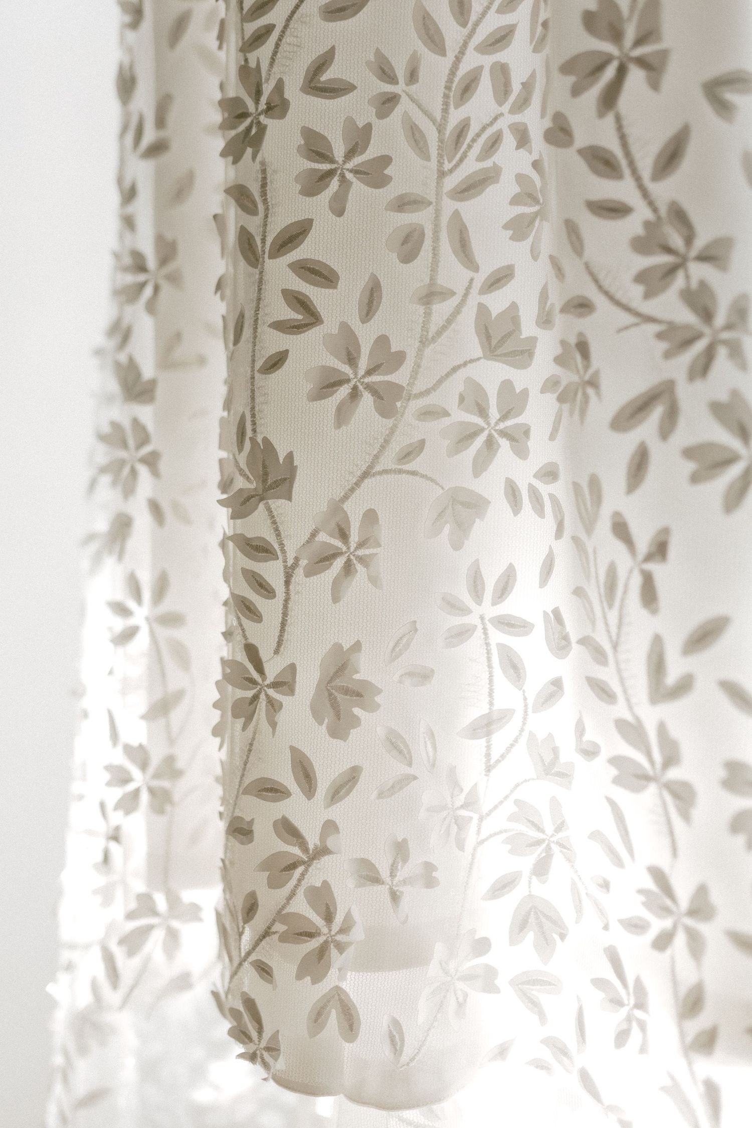 Delicate floral pattern on sheer white curtain fabric with soft natural lighting.