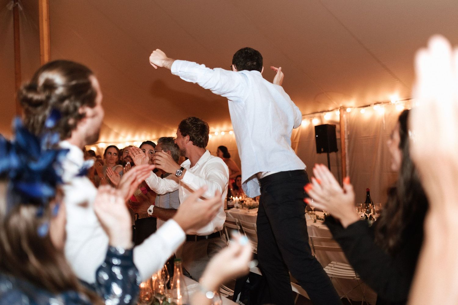 Energetic wedding reception scene with dancing guests under warm string lights in a tent.