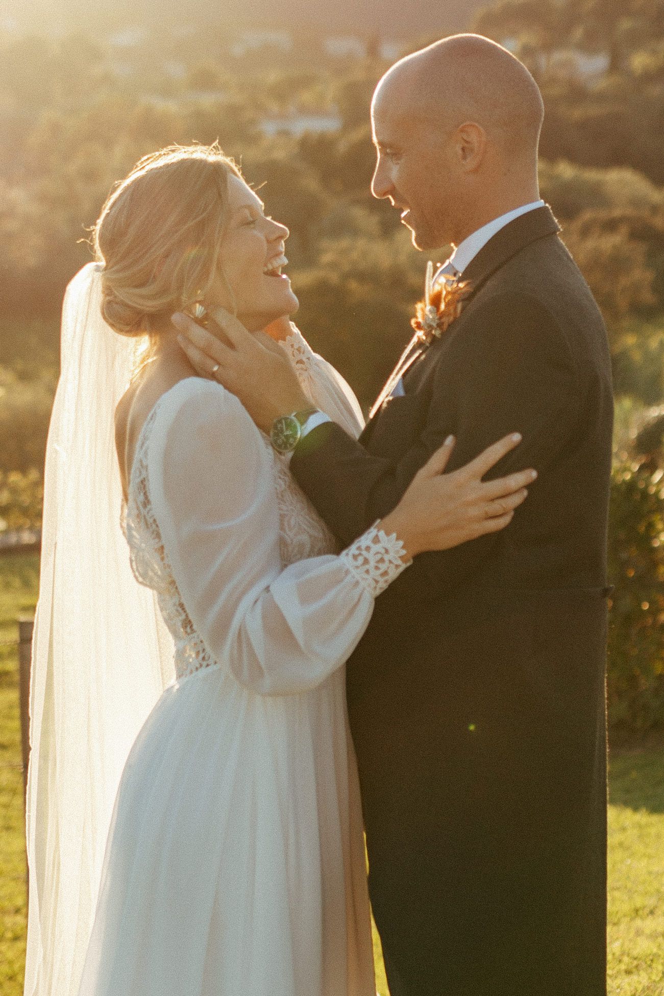 Newlywed couple sharing an intimate moment at sunset in a garden setting while dressed in wedding attire.