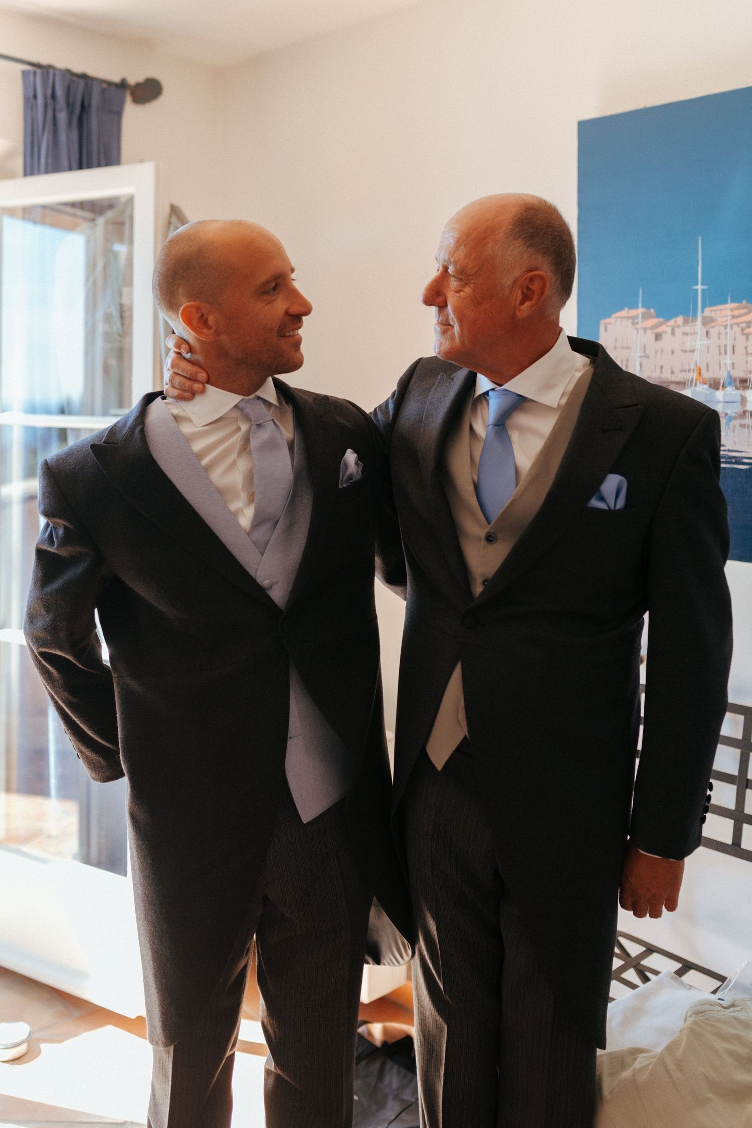 Two men in formal wedding attire sharing an emotional moment indoors.