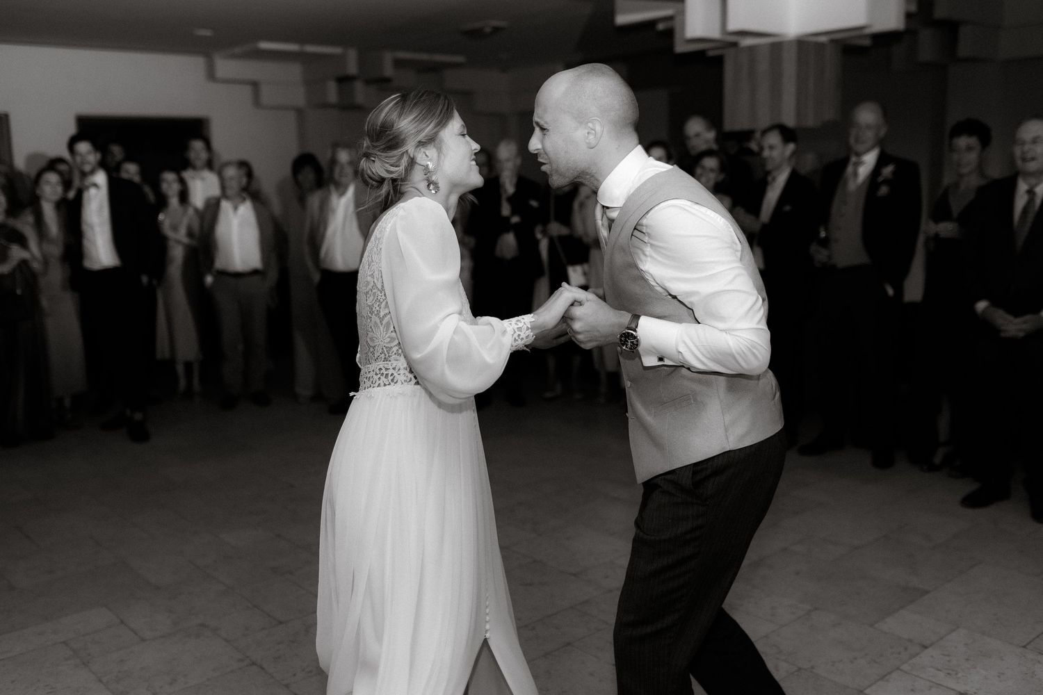 Black and white photo of newlyweds dancing energetically at their reception.