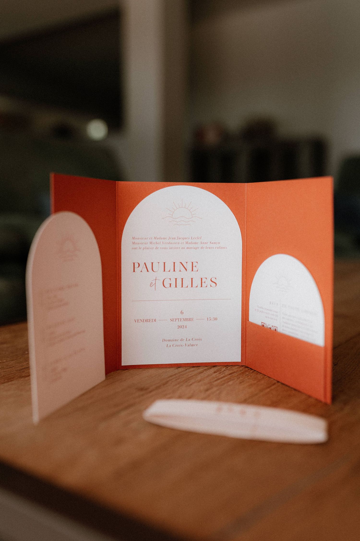 Peach-colored wedding invitation with arched design displayed on wooden surface in warm lighting.