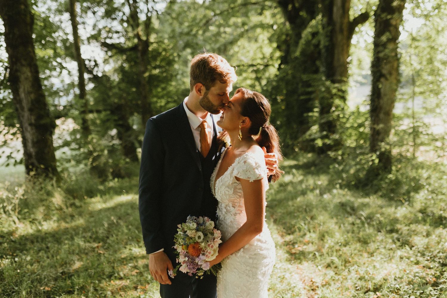 A romantic wedding moment captured in golden sunlight among trees.