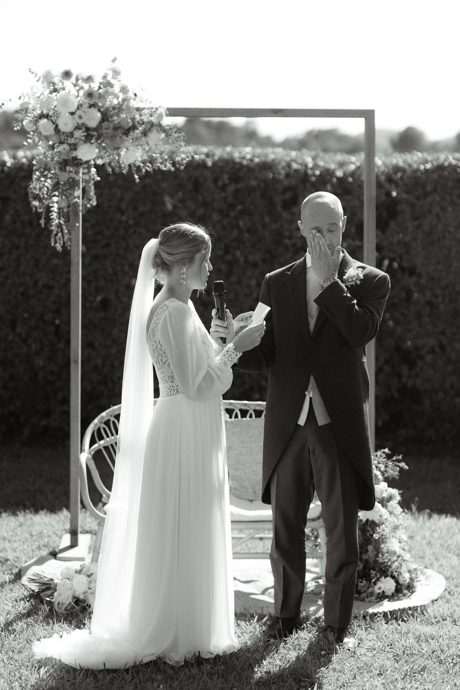 A couple sharing an emotional moment during their wedding ceremony under a floral-decorated wooden arch.