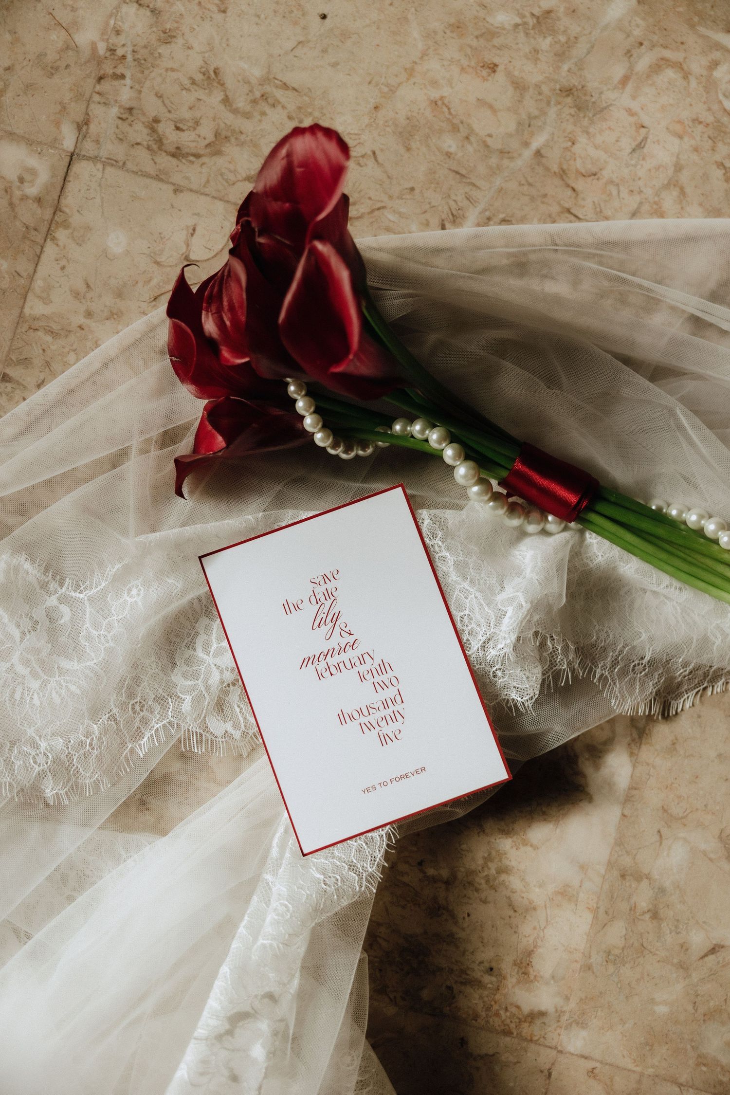 Red calla lilies and wedding invitation card lay delicately on lace veil.