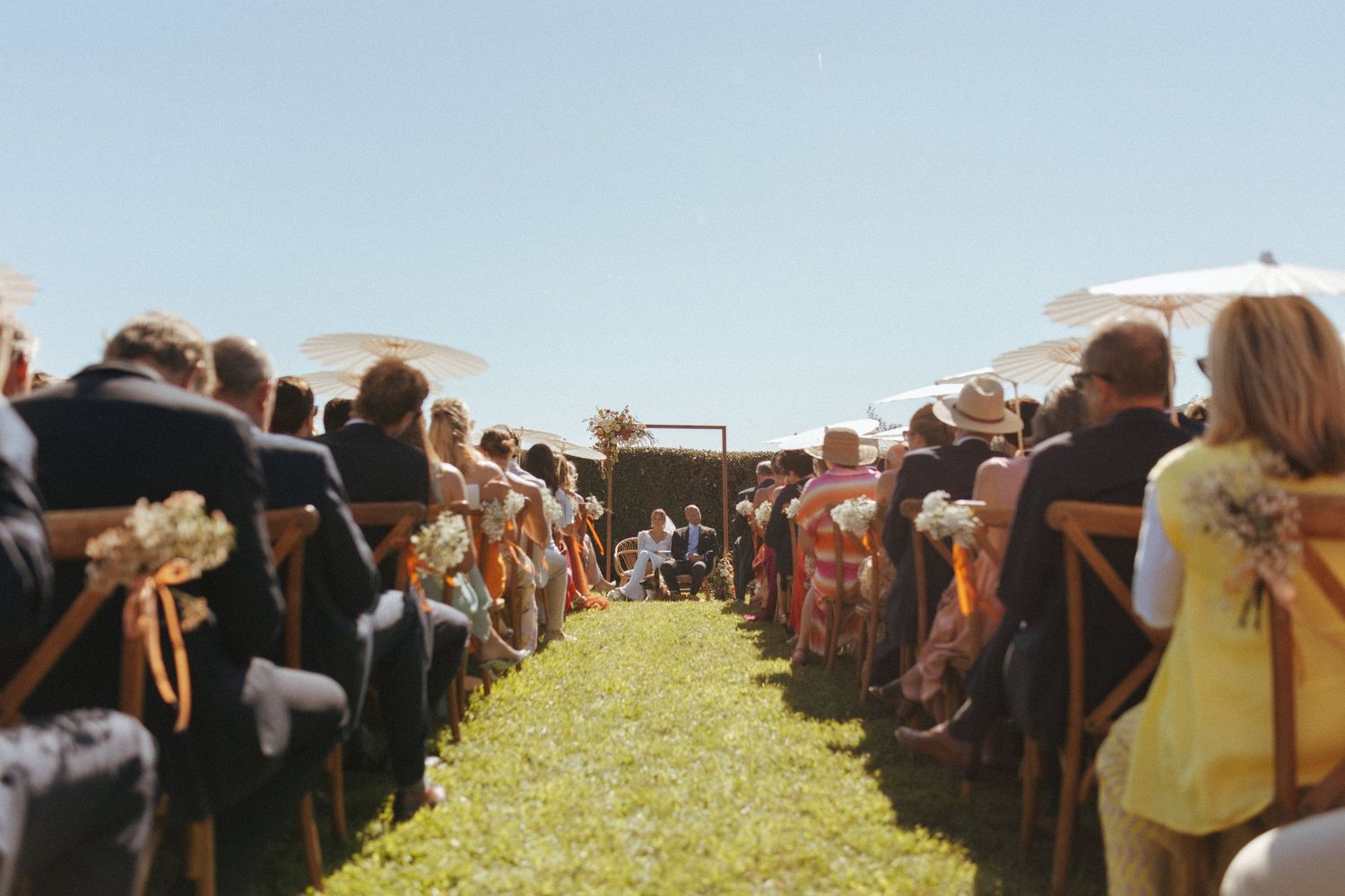 Outdoor wedding ceremony seating arrangement with rows of guests under clear blue skies.
