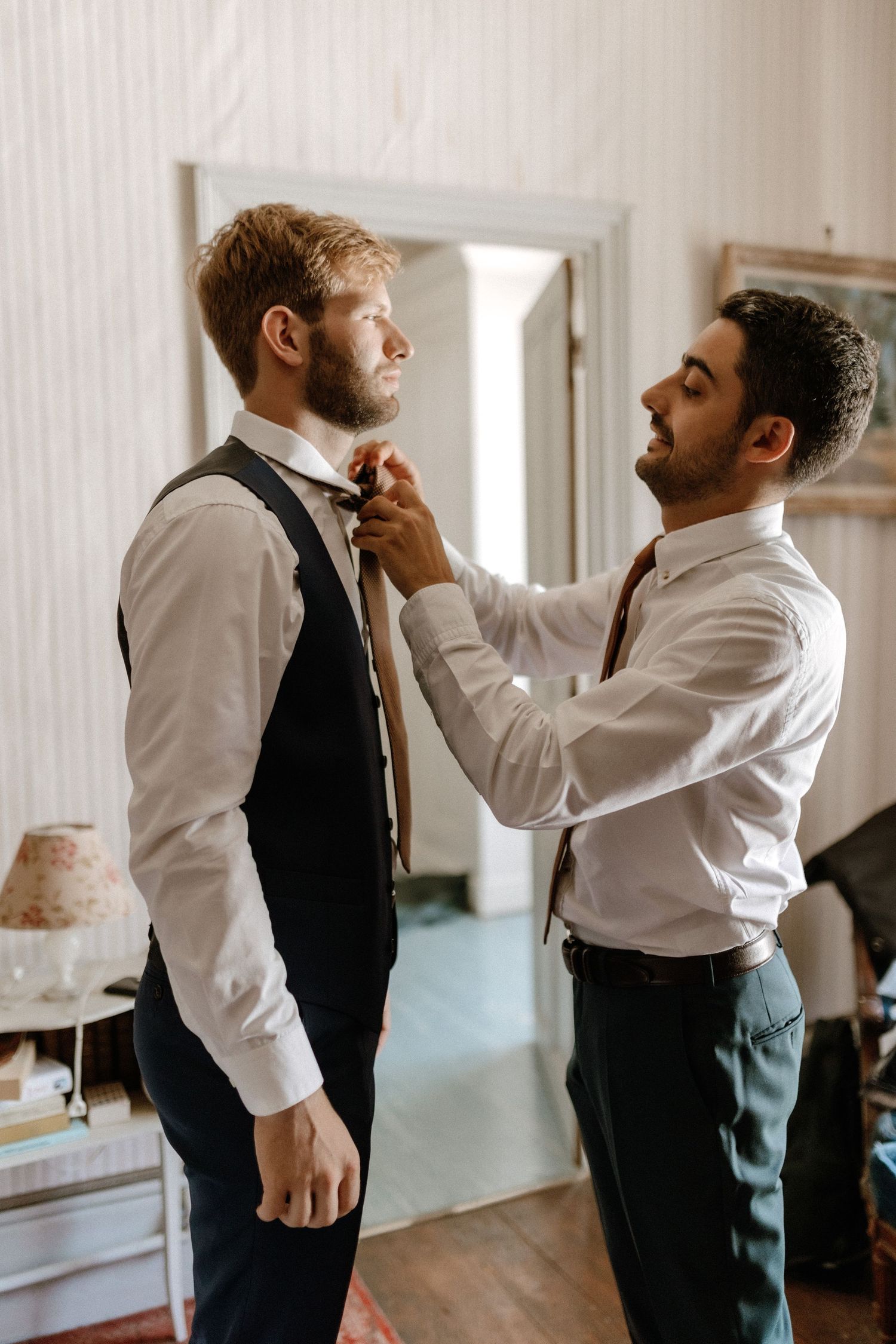 Two people in formal attire helping with wedding preparations indoors.