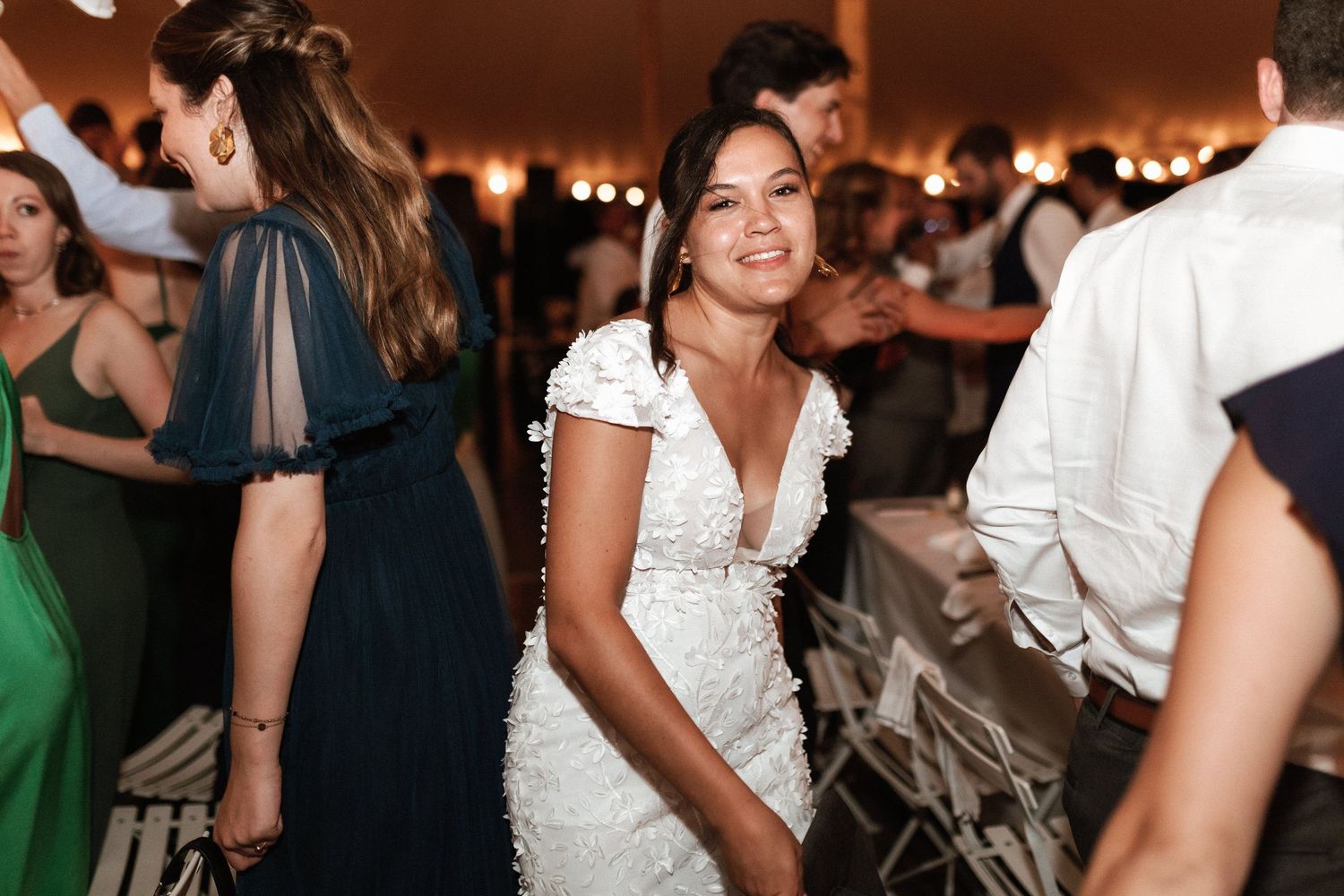 Wedding celebration with guests dancing and mingling under warm tent lighting.