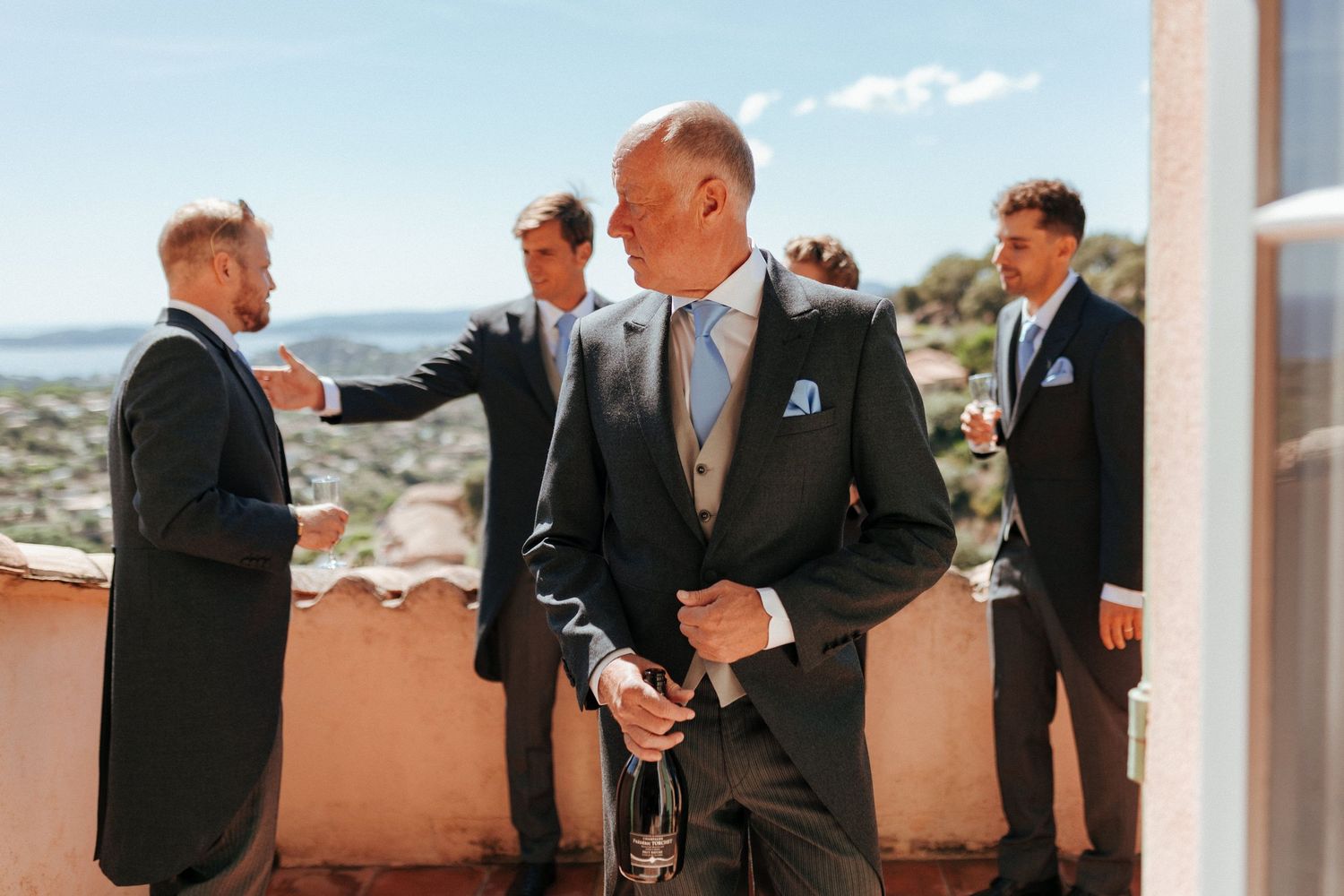 Groomsmen in dark suits gathering on a terrace with mountain views.