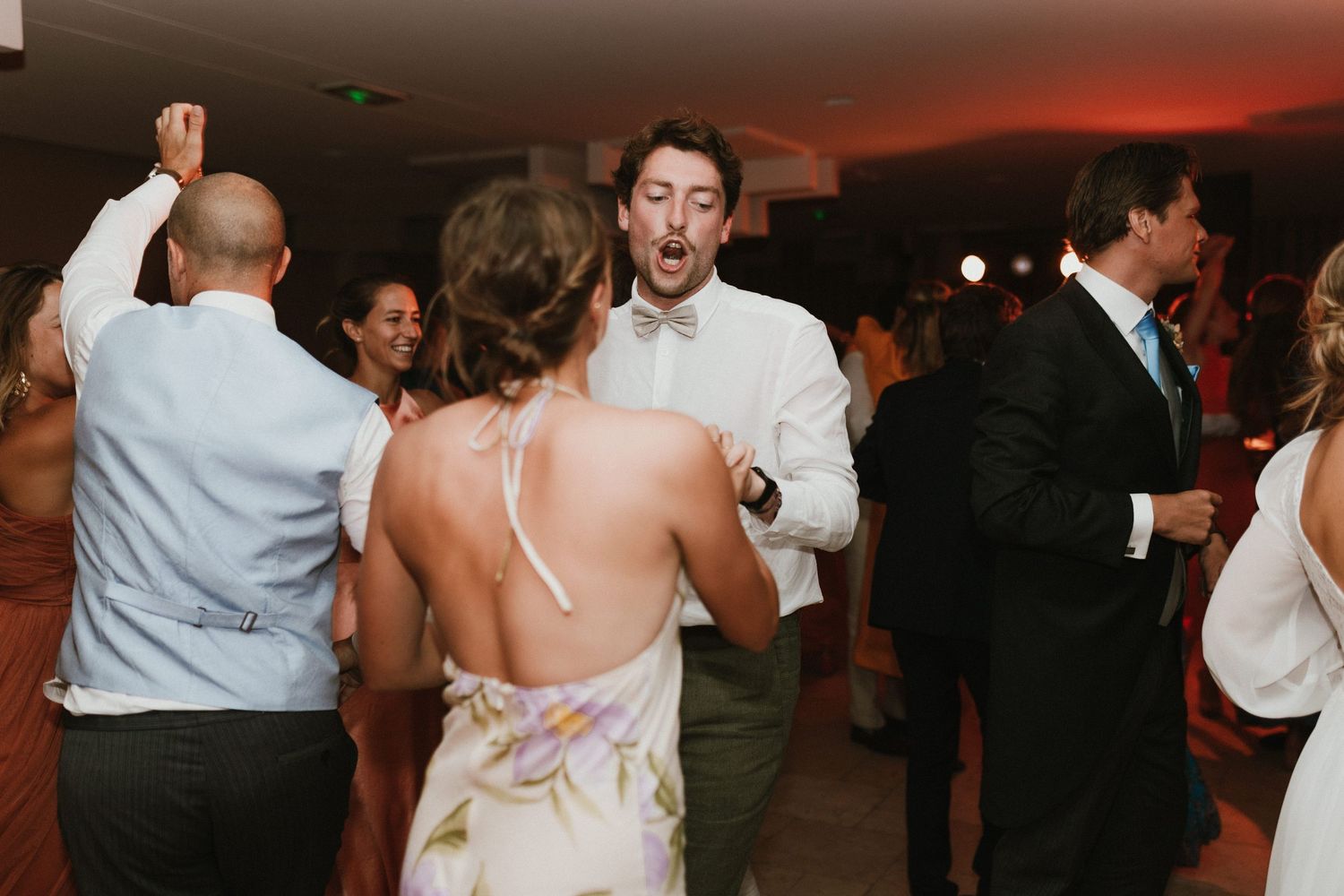 Wedding guests dancing and celebrating on illuminated dance floor at reception.