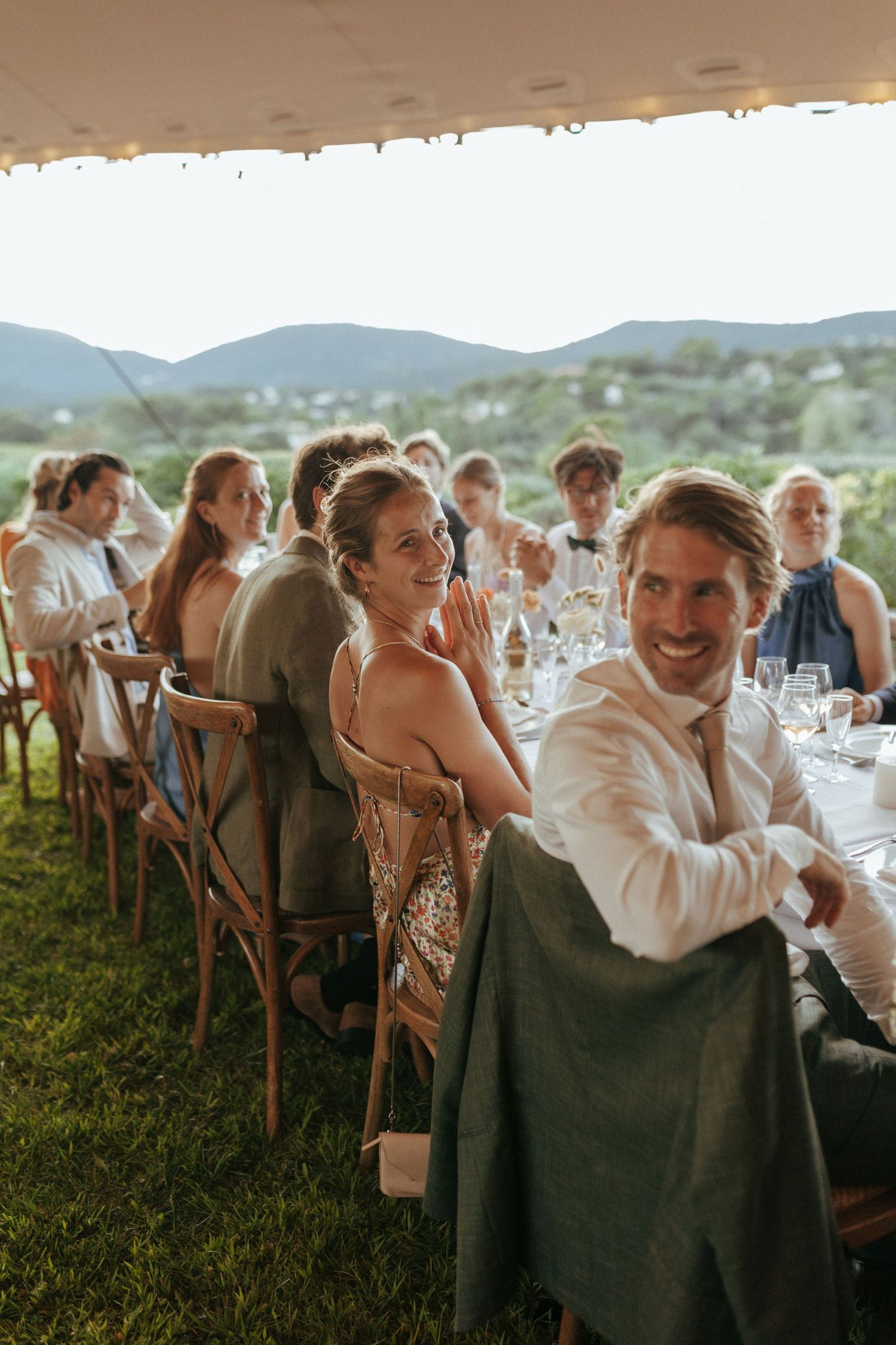 Wedding reception guests dine at long tables under outdoor tent with mountain views.