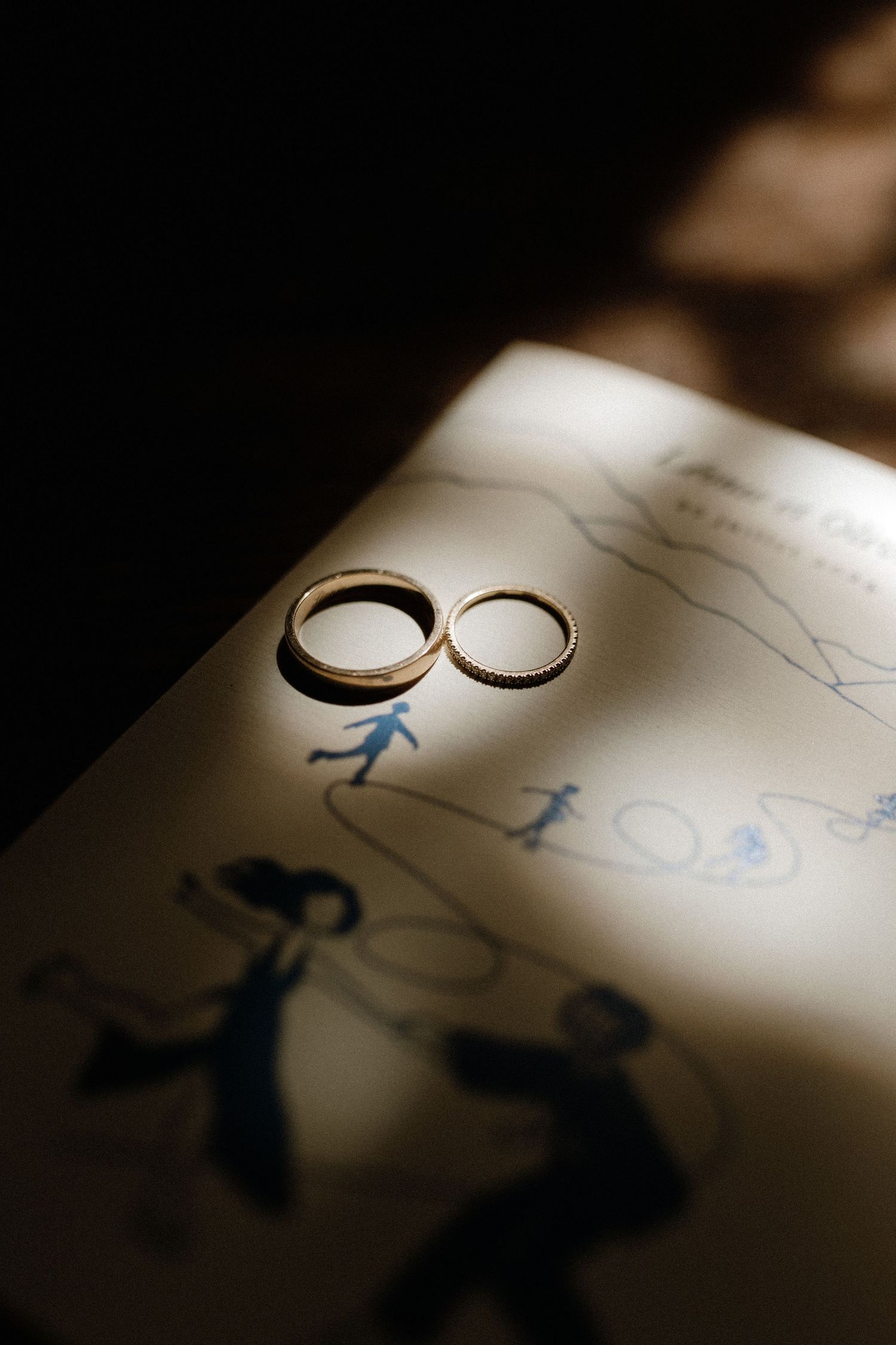 Wedding rings cast shadows on paper with stick figure drawings creating an artistic composition.