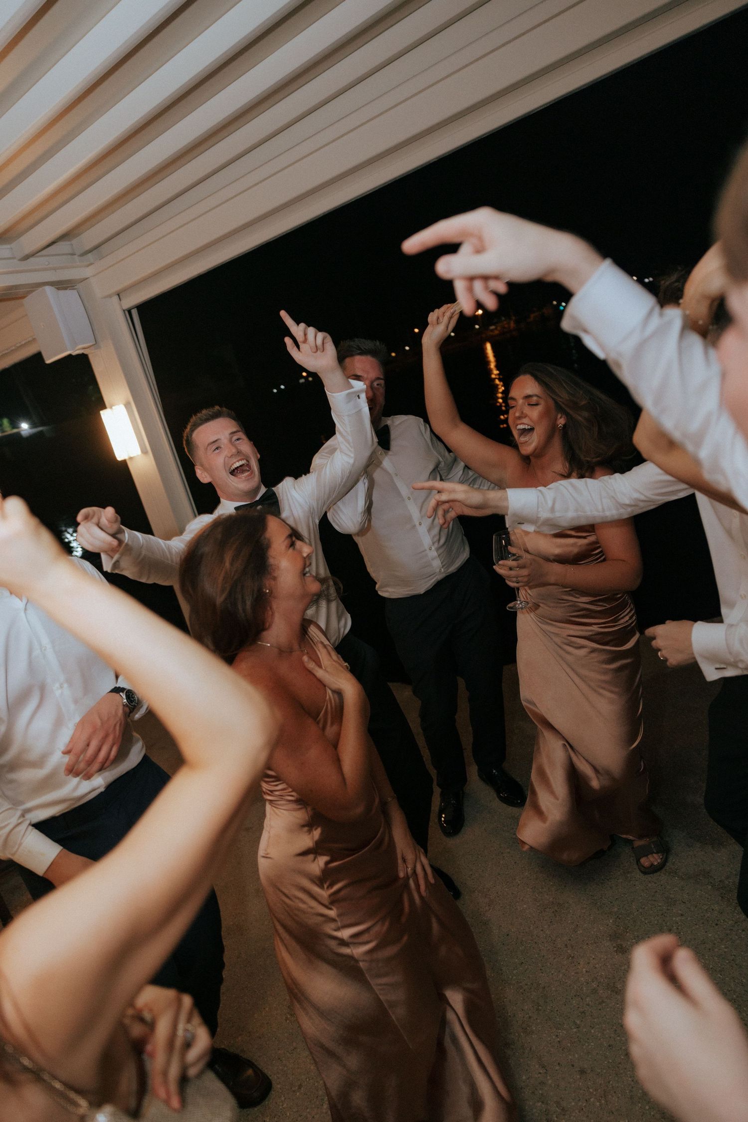 Wedding guests dance energetically at a reception party with people in brown dresses and white shirts having fun.