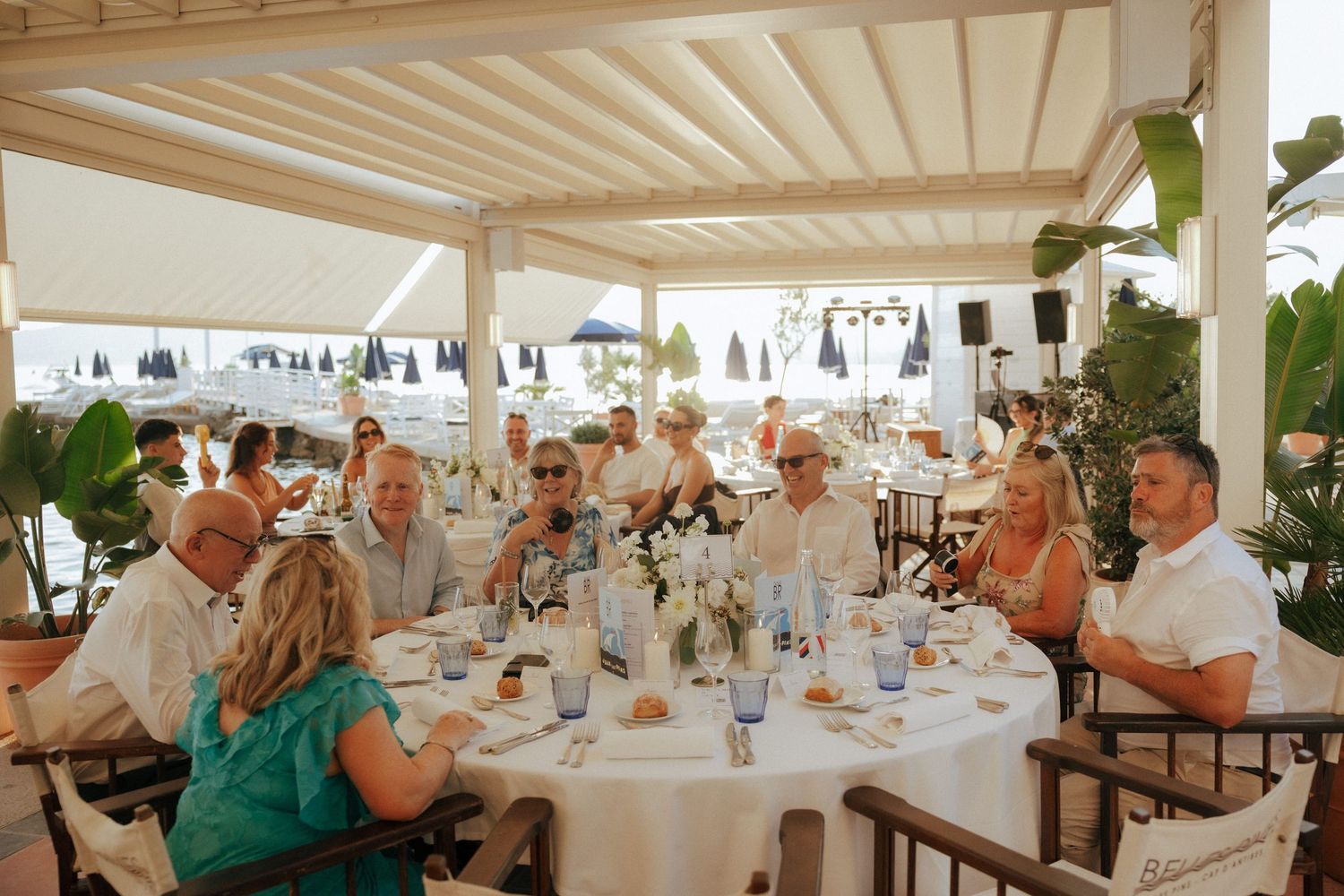 Panoramic view of a wedding reception with white table settings under a covered outdoor venue with white columns and decor.