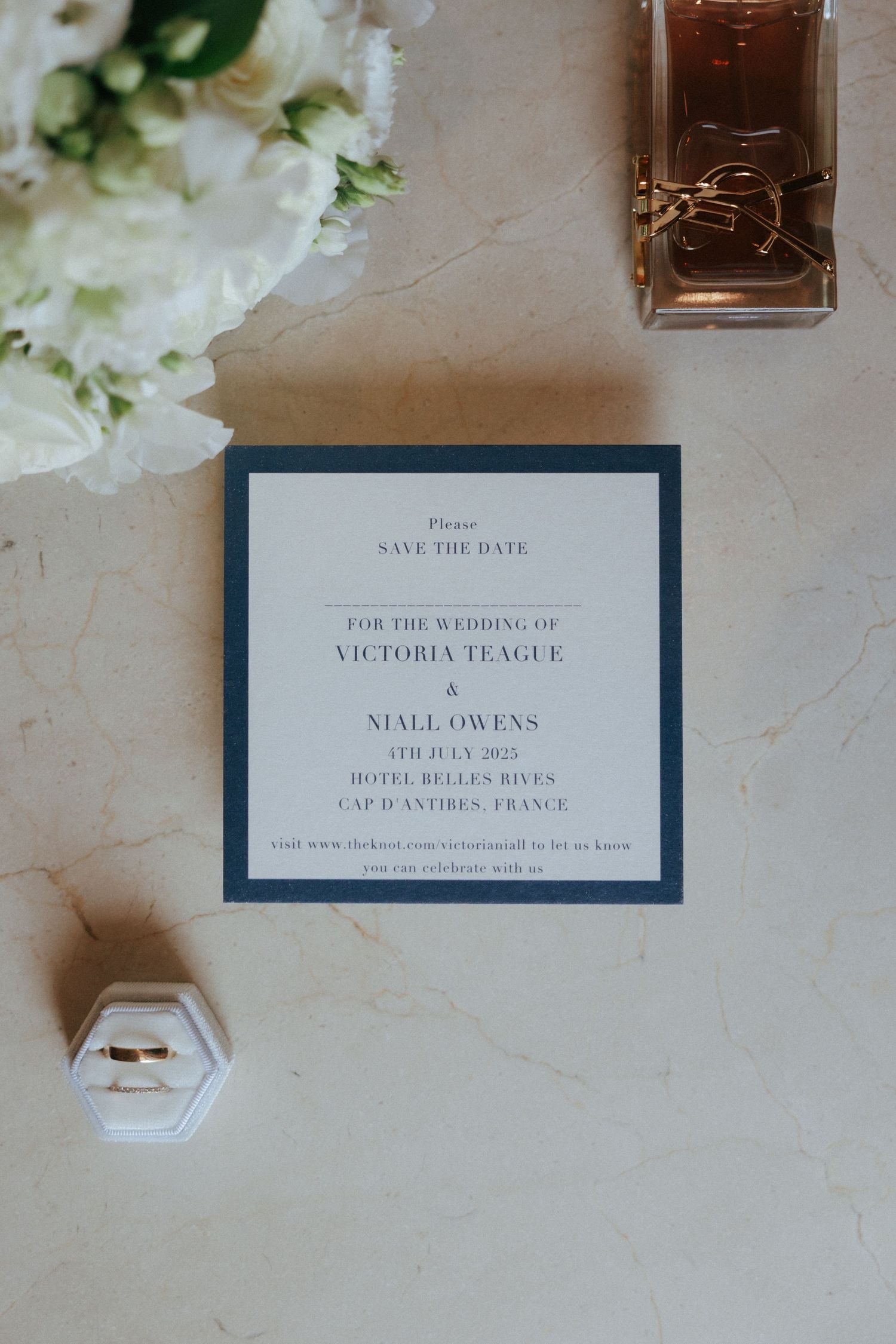 Elegant wedding save-the-date invitations in navy blue and white with floral decor on a beige textured surface.