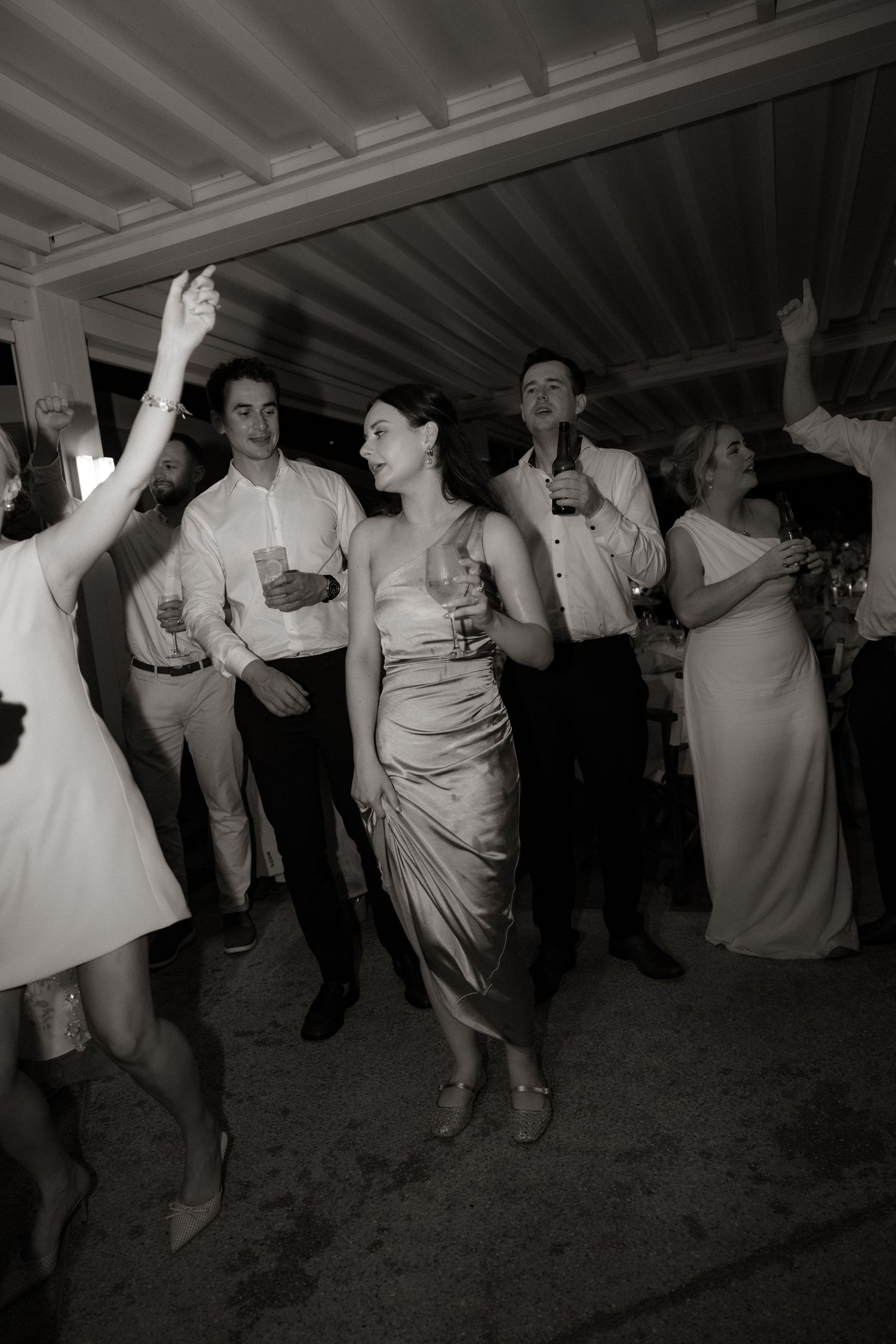 Black and white photo of wedding guests dancing and celebrating at an indoor party.
