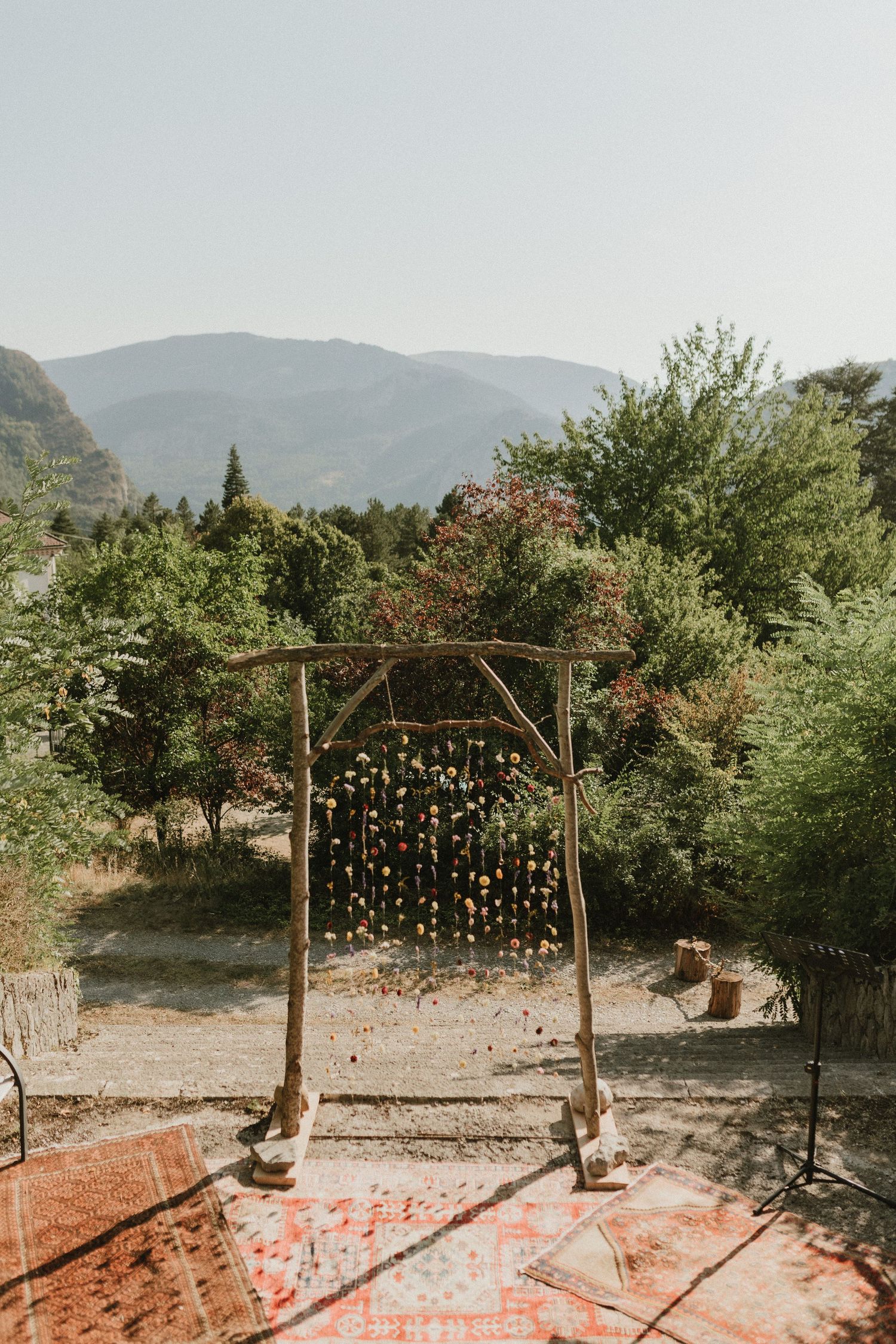 Rustic wooden arch adorned with hanging lights creates a romantic backdrop against rolling mountain hills in golden sunlight.