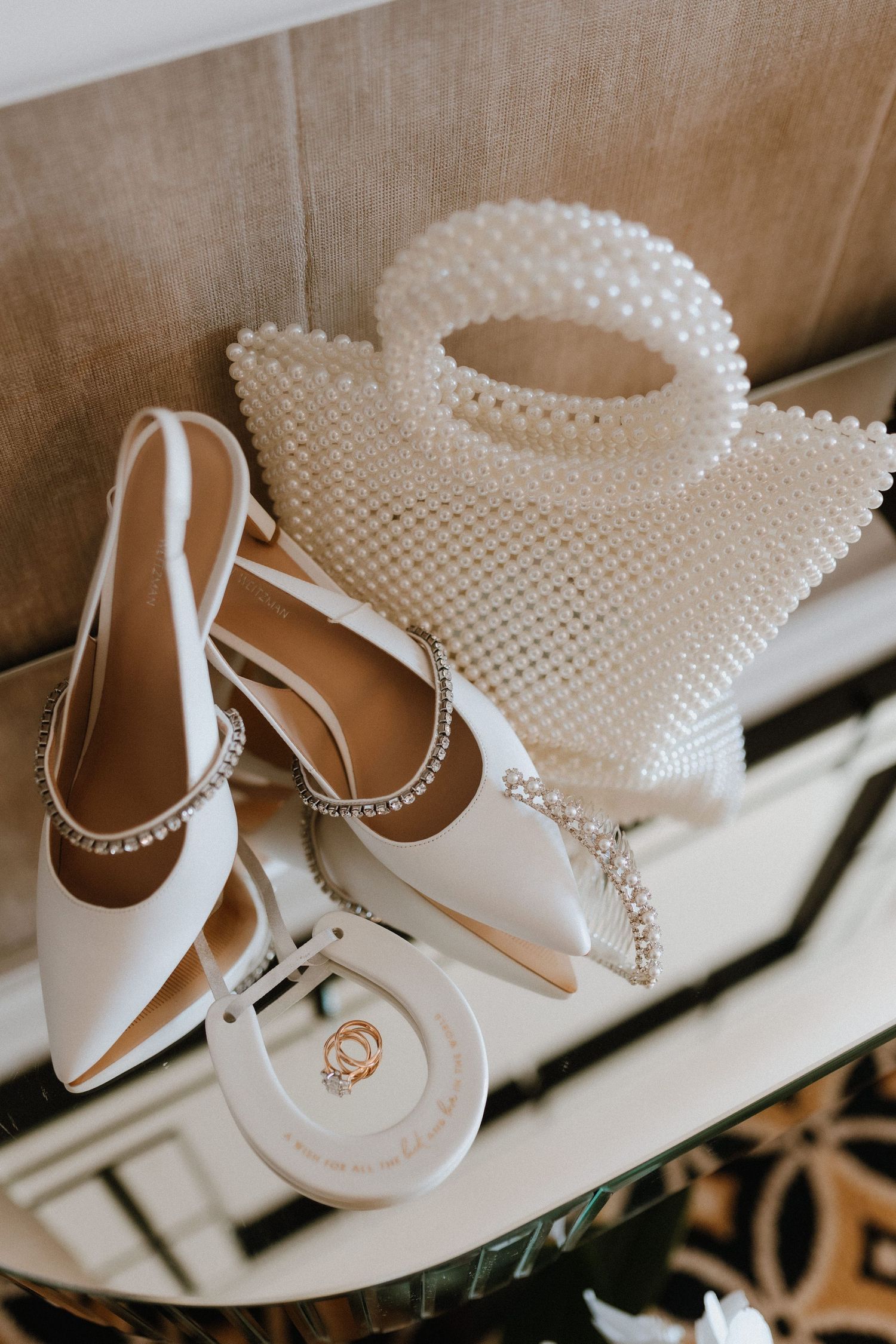 Elegant white bridal accessories including pearl beaded handbag, slingback heels, and small ring box on a light surface.