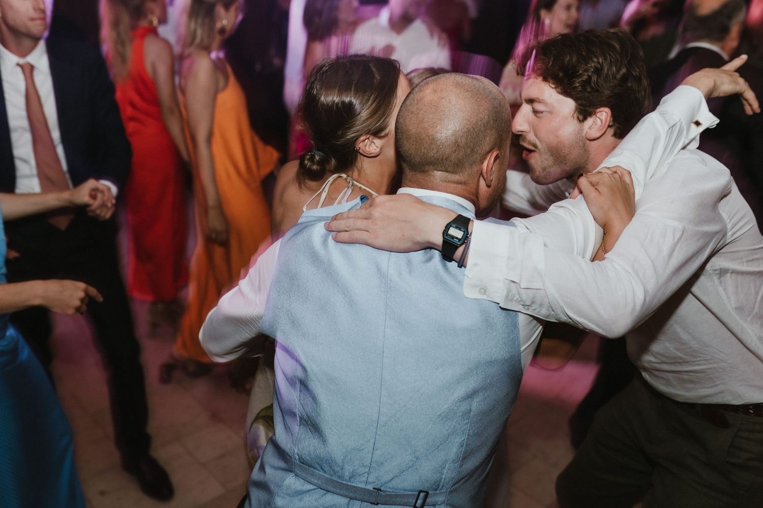 People dancing and embracing enthusiastically on a lively wedding reception dance floor.