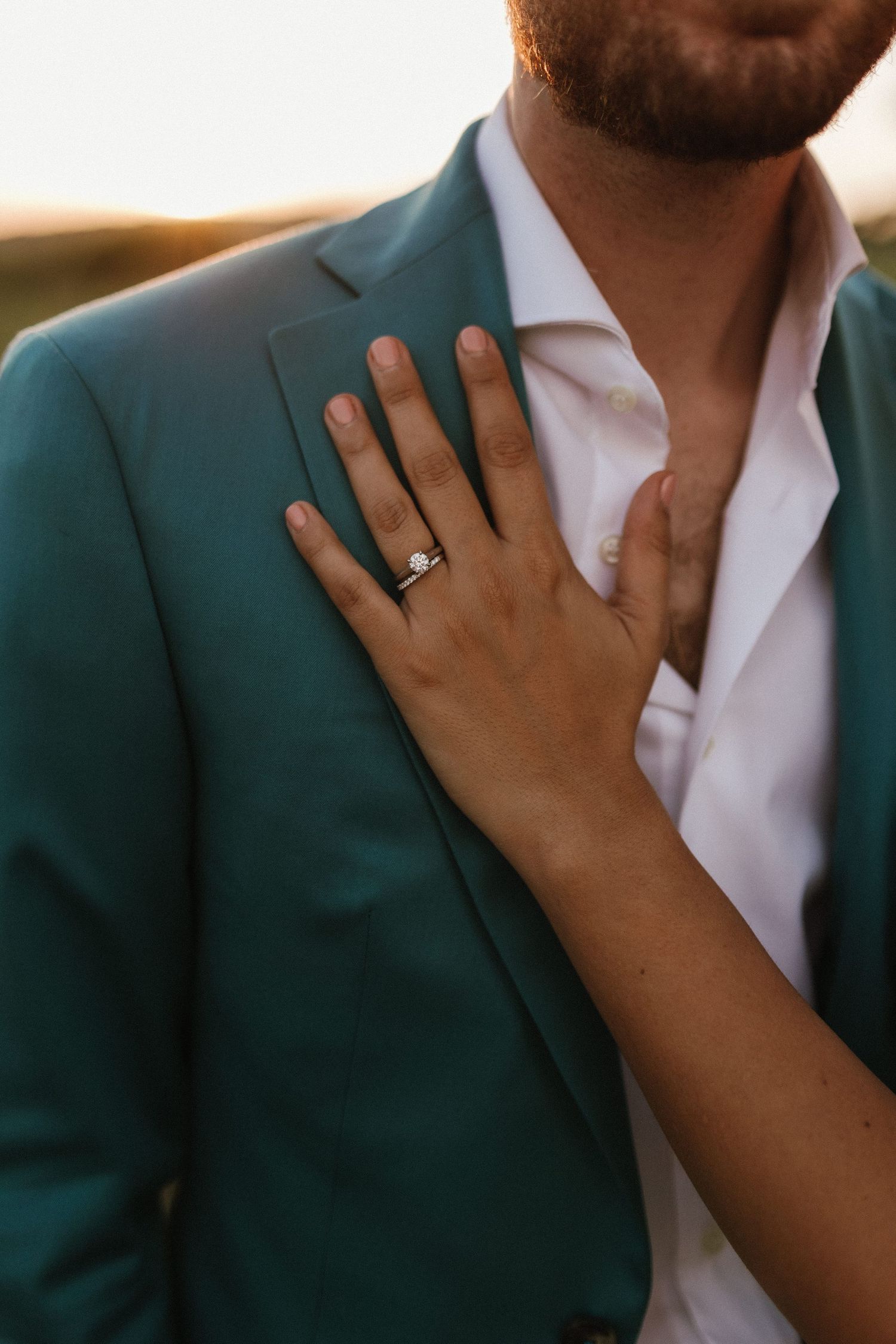 A close-up of a wedding ring on hand against a teal suit jacket.