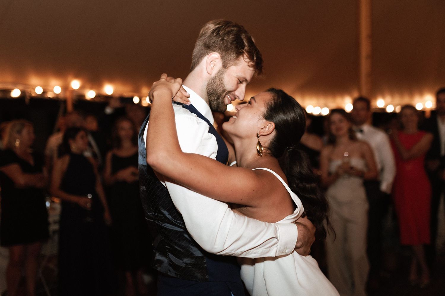 A couple shares their first dance at their wedding reception with glowing lights in the background.