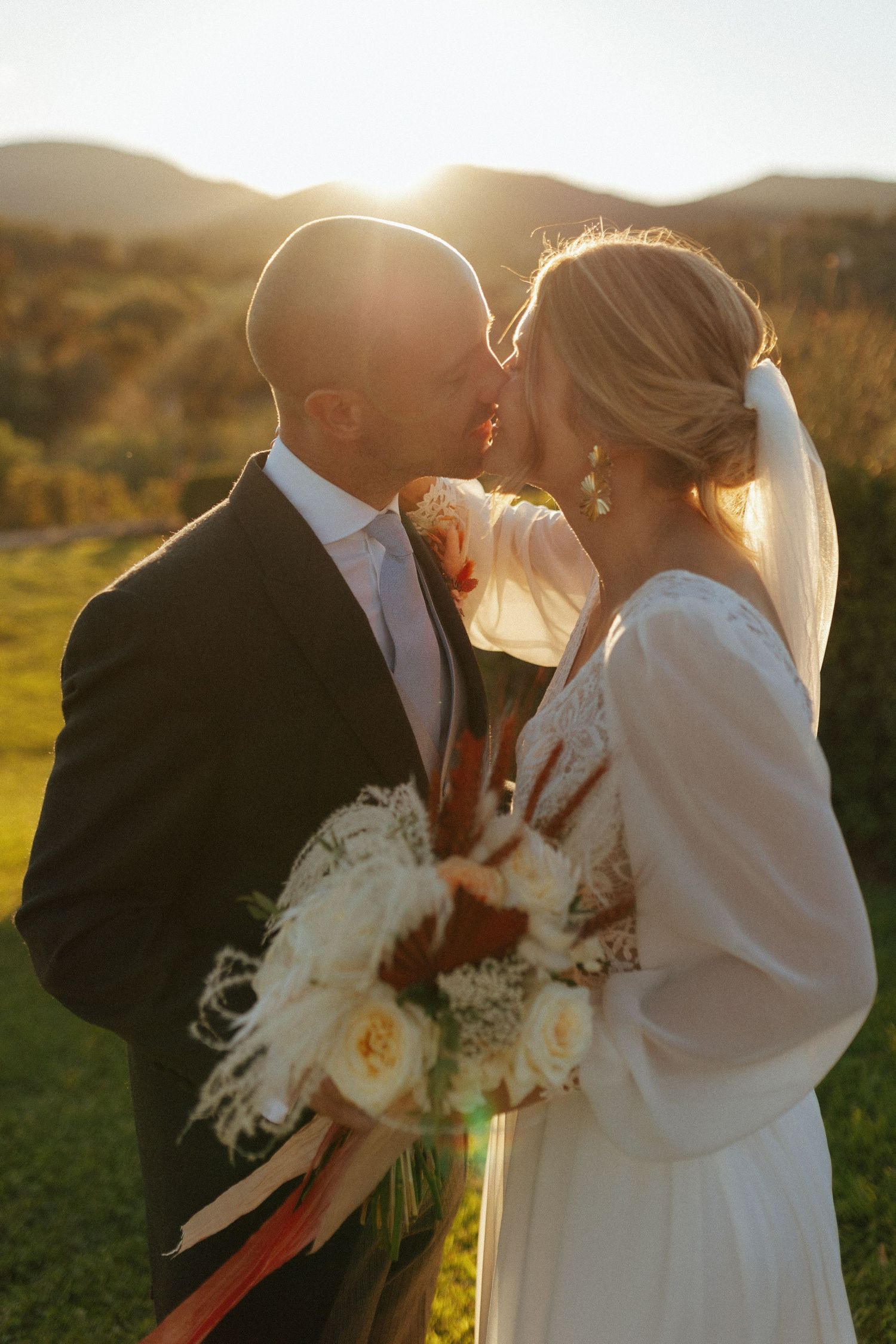 A couple shares an intimate moment during their sunset wedding ceremony against a mountainous backdrop.